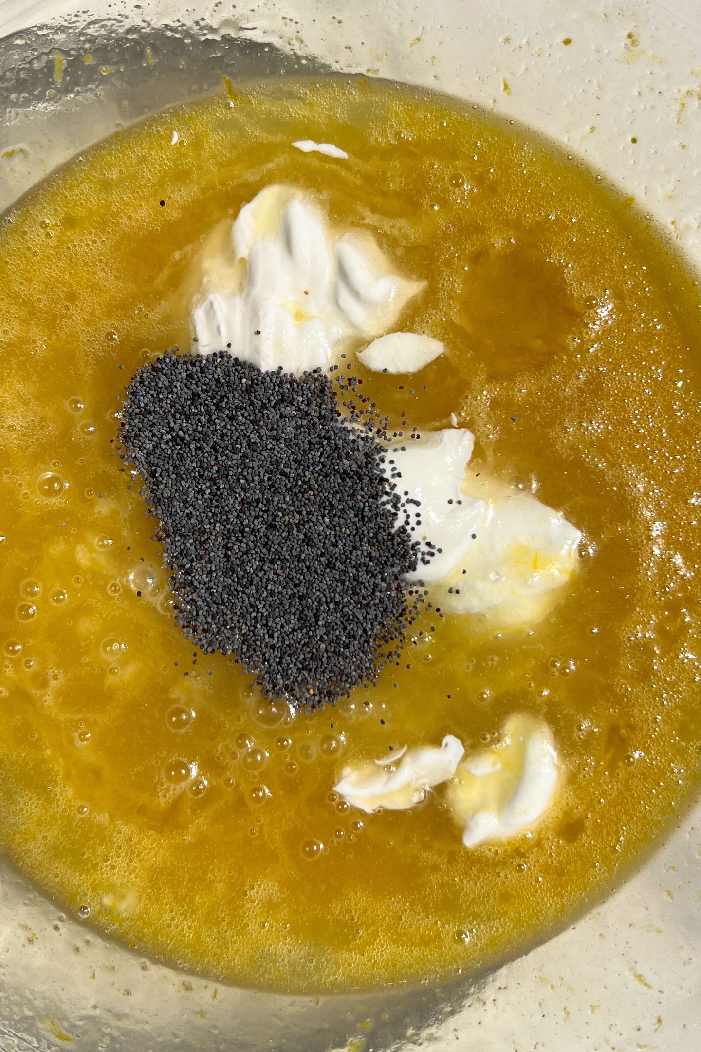 Wet ingredients for the cupcake batter in a bowl with poppy seeds.