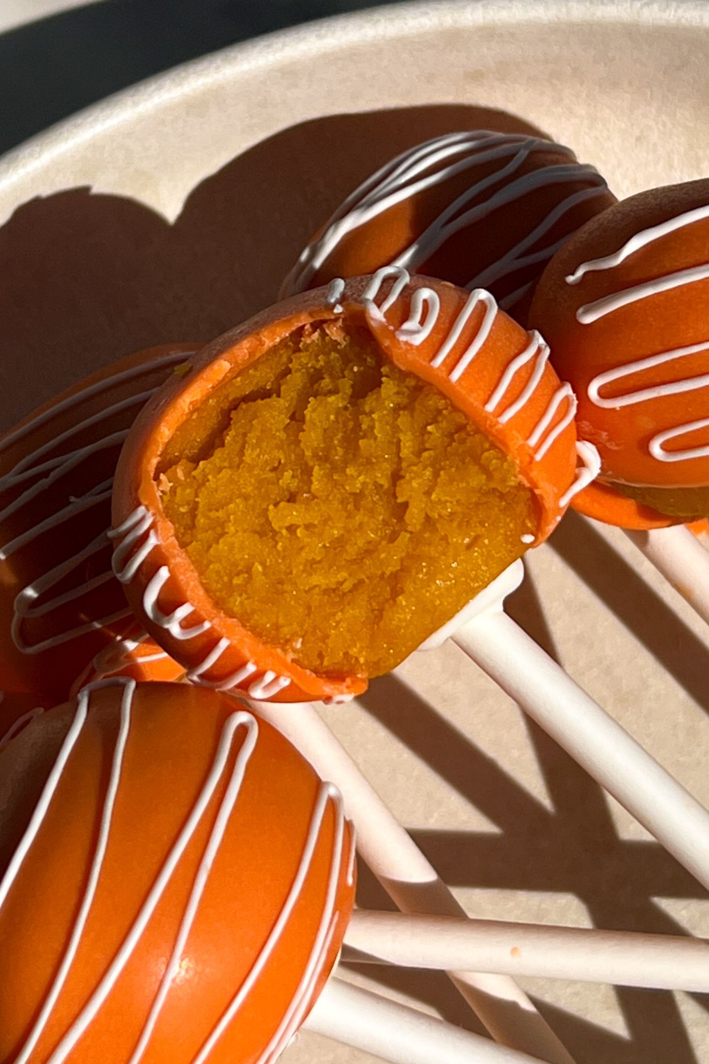 Orange cake pop with a bite taken out of it.