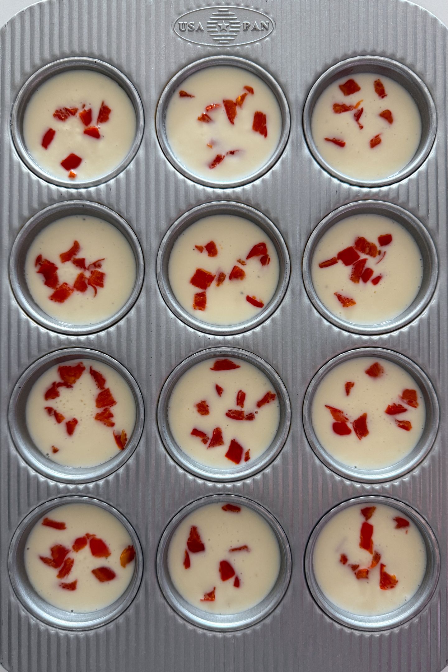Egg White Bites batter with diced red bell peppers in the muffin tin.