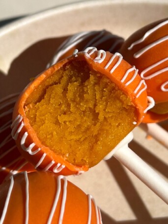 Orange flavored cake pop with a bite taken out of it.