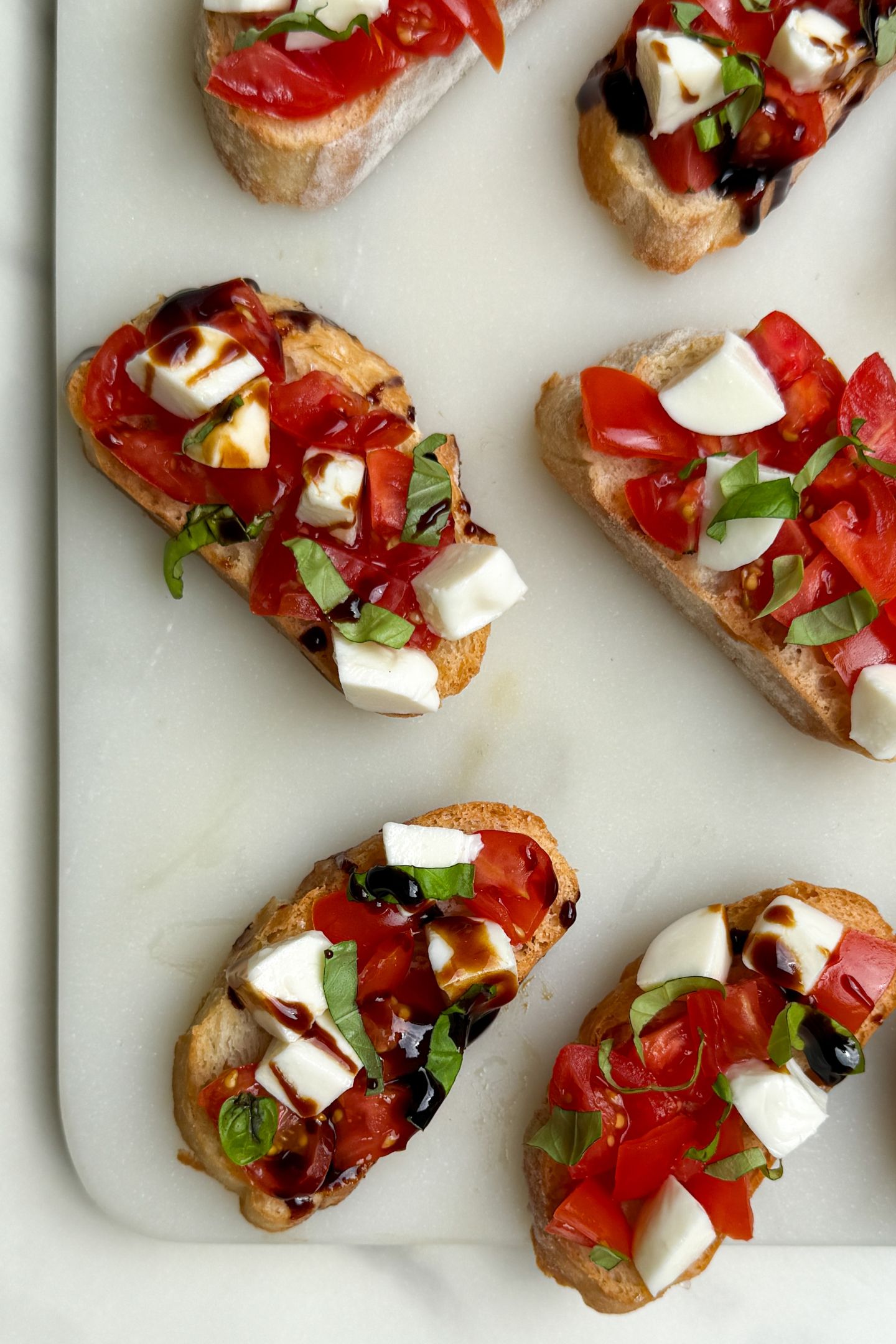 Prepared Caprese Crostinis on a platter with balsamic glaze drizzle.