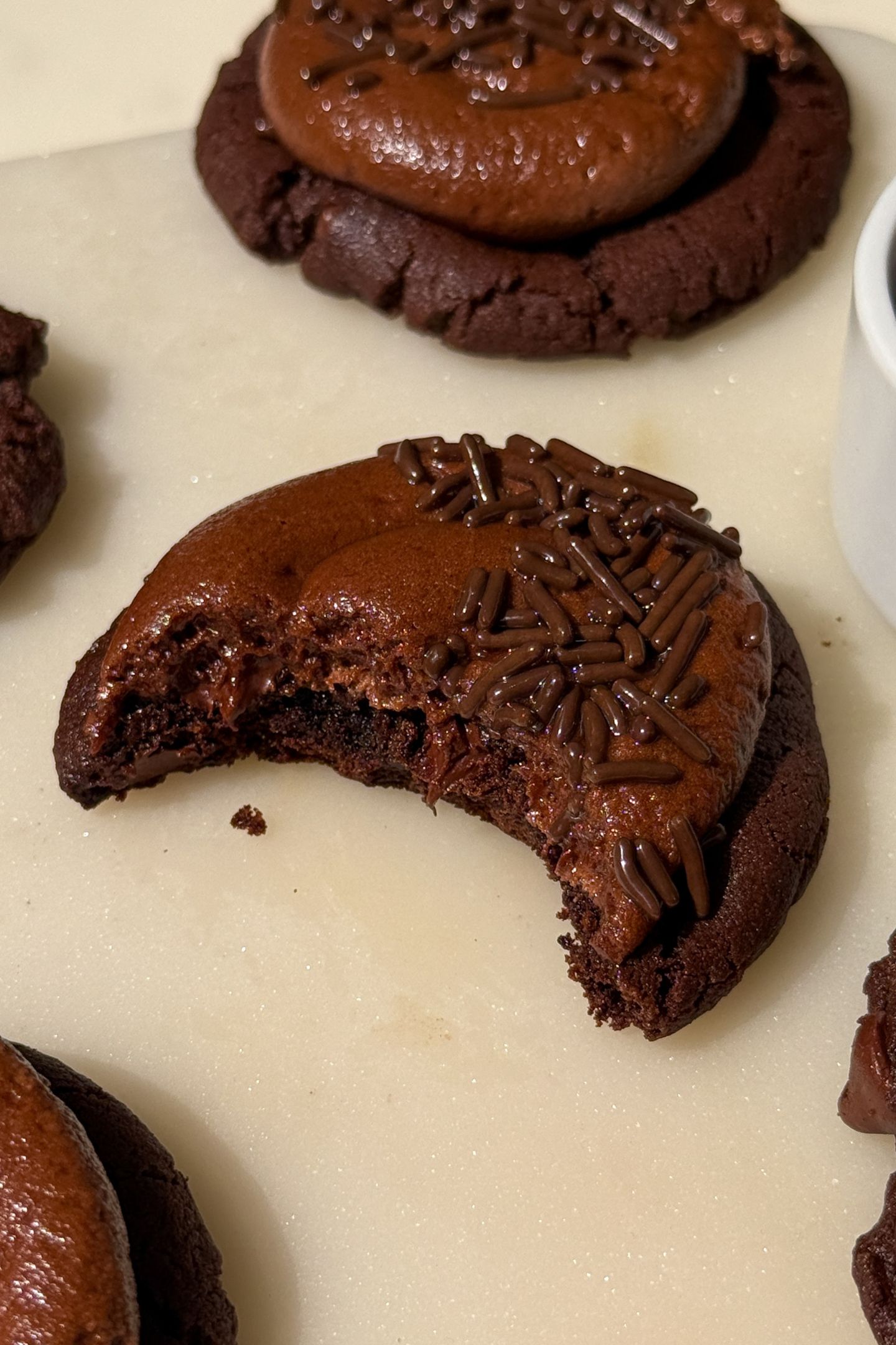 A frosted chocolate chocolate chip cookie with a bite taken out of it.