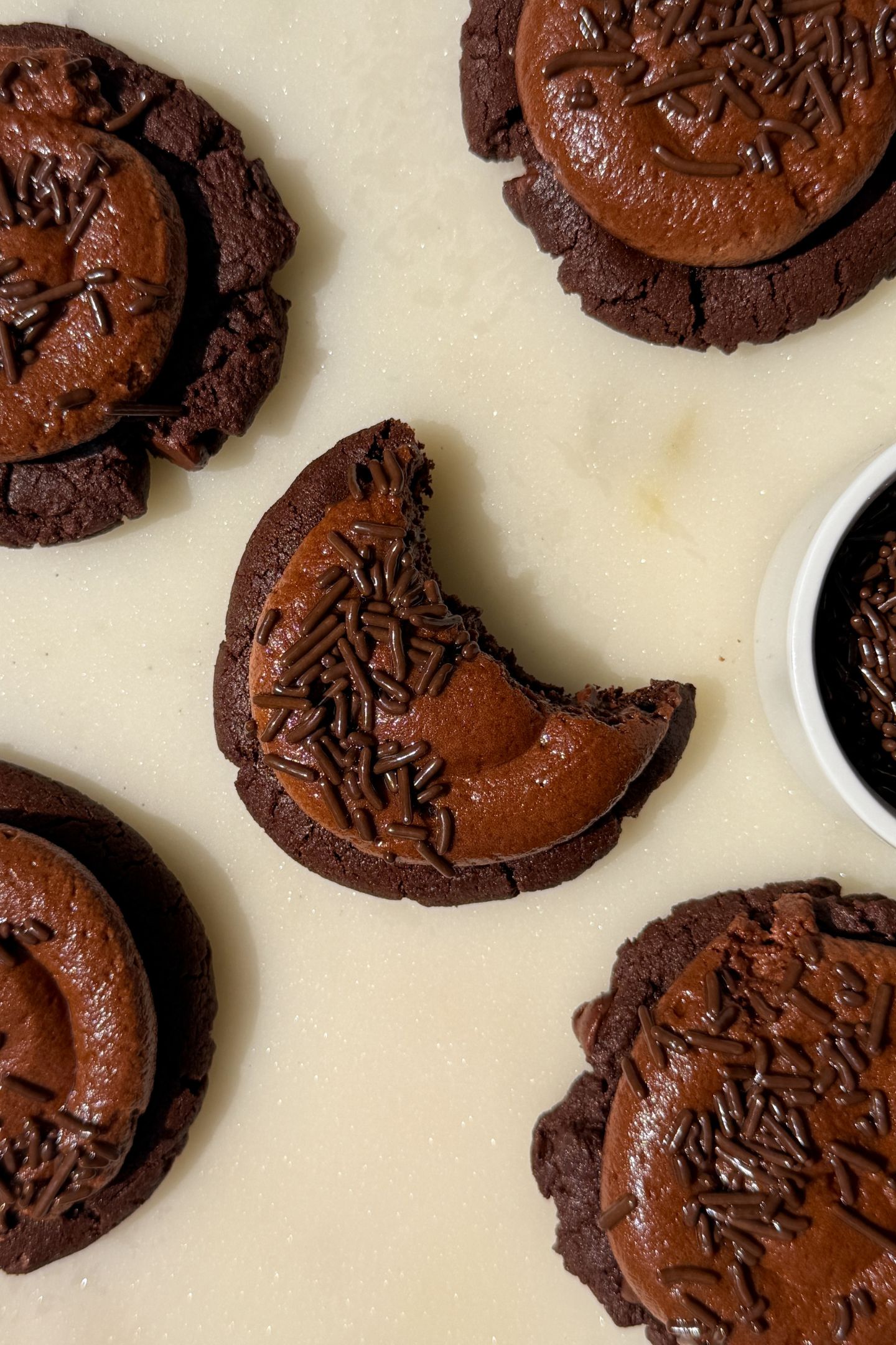Frosted Chocolate cookies on a platter with one having a bite taken out of it.