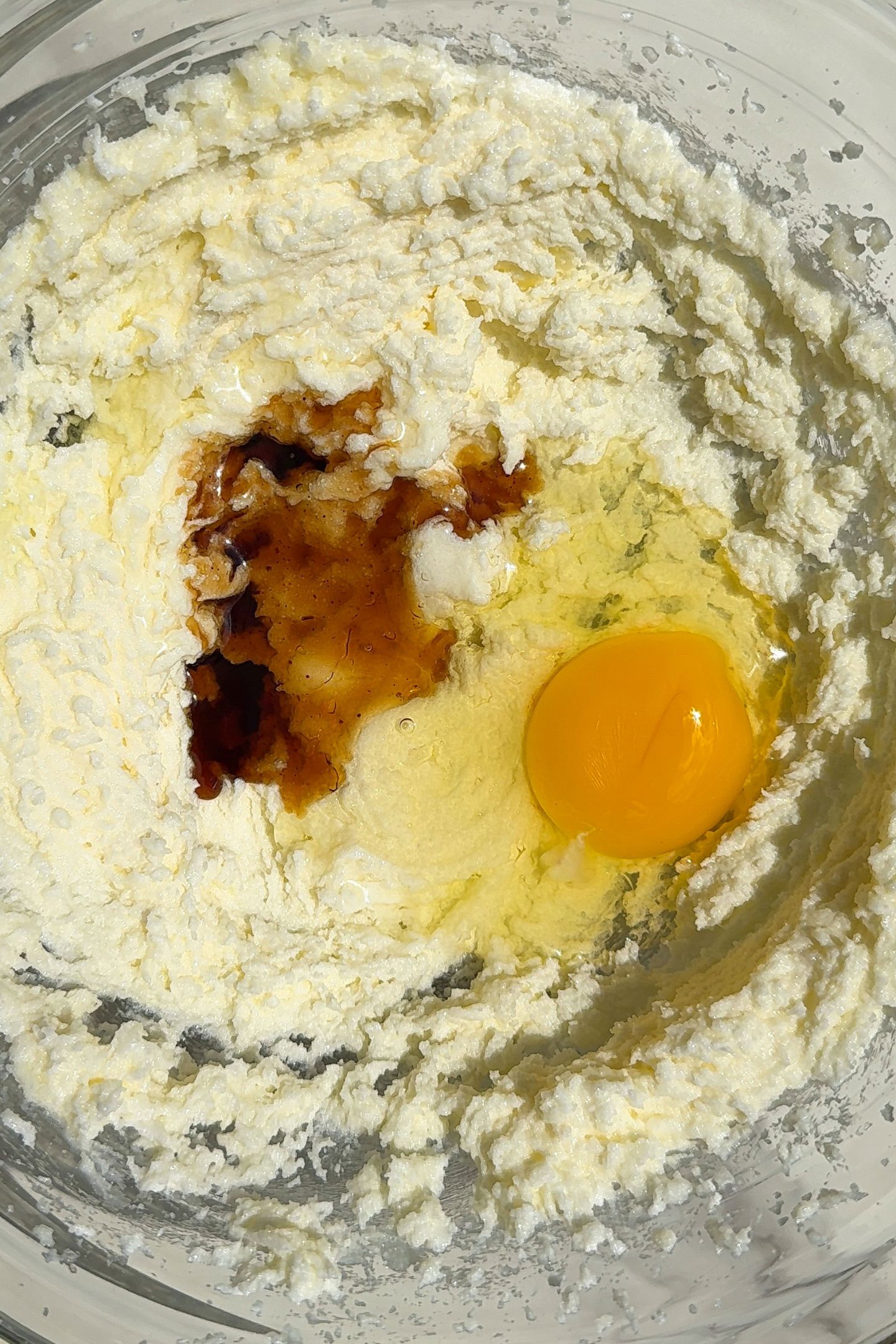 Butter and sugar creamed together in a bowl topped with vanilla extract and an egg.