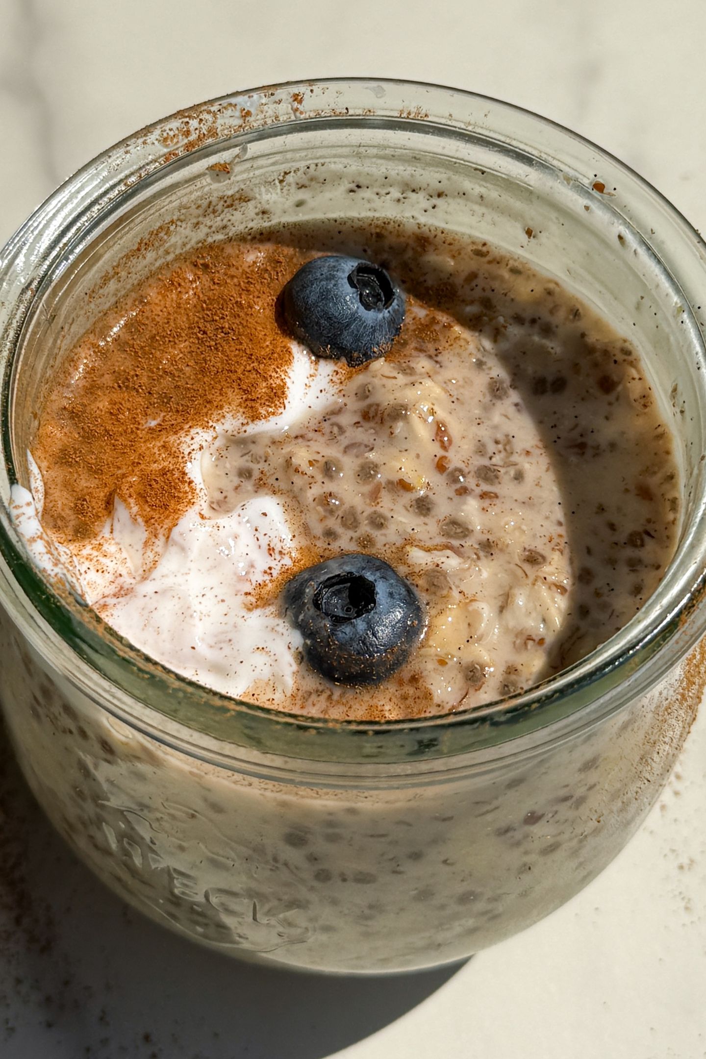 Maple and Brown Sugar Oatmeal in a mason jar topped with yogurt, cinnamon and fresh blueberries.