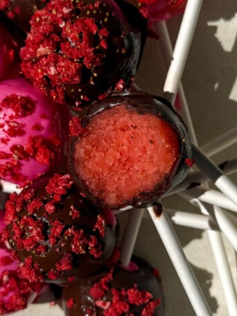 Strawberry cake pop with a bite taken out of it on a platter with other cake pops.