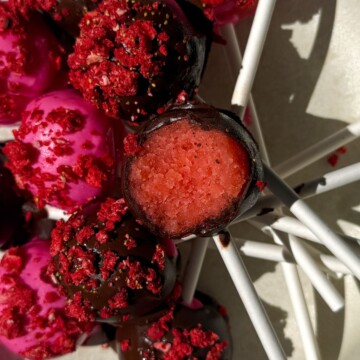 Strawberry cake pop with a bite taken out of it on a platter with other cake pops.