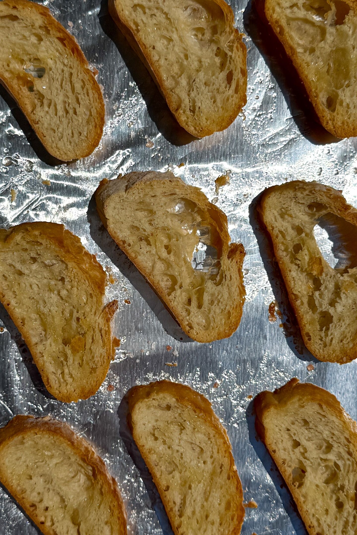 Baked crostini slices on a prepared baking sheet lined with aluminum foil.
