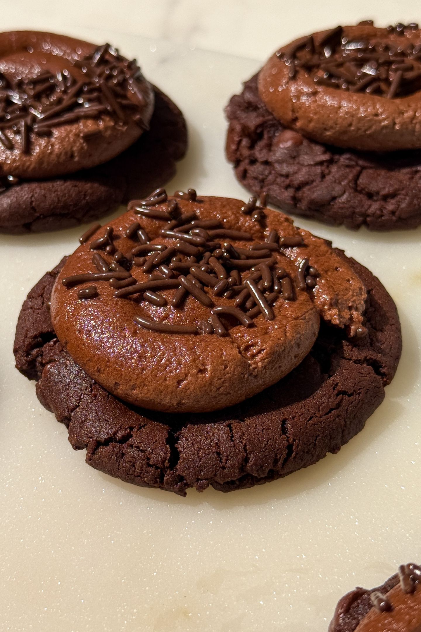 A chocolate cookie topped with a chocolate buttercream frosting and sprinkles.
