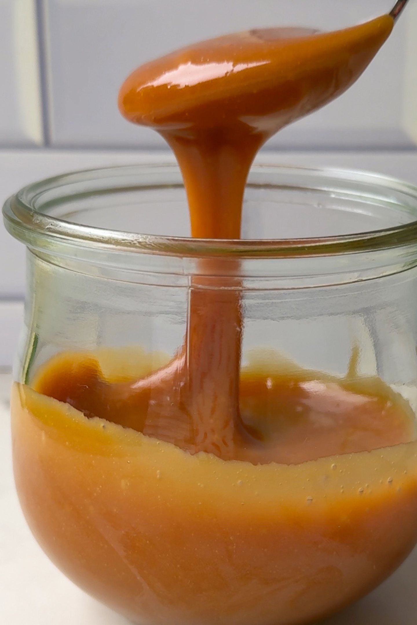 Caramel drizzling off of a spoon into a glass jar.