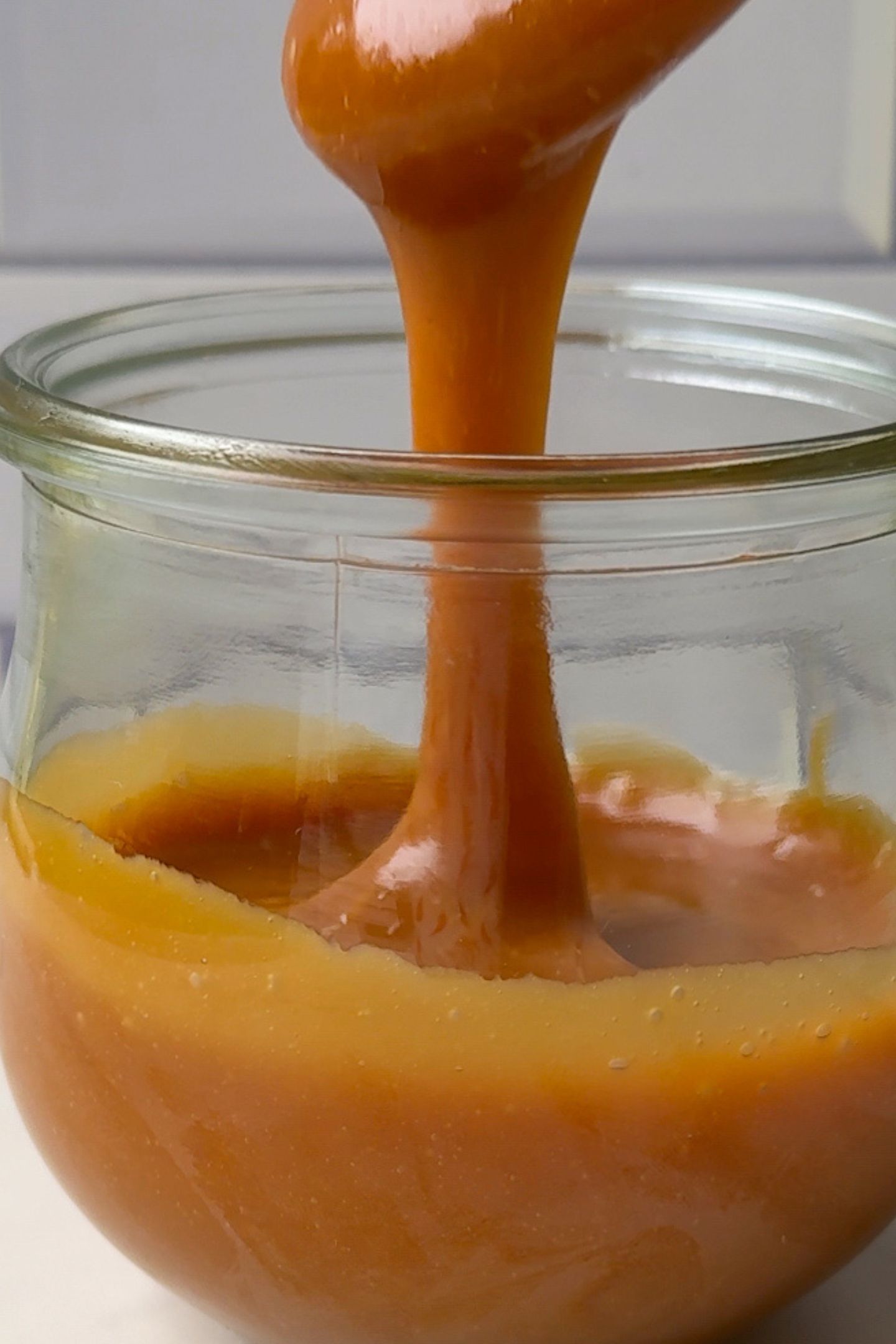 Caramel drizzling off of a spoon into a glass jar.