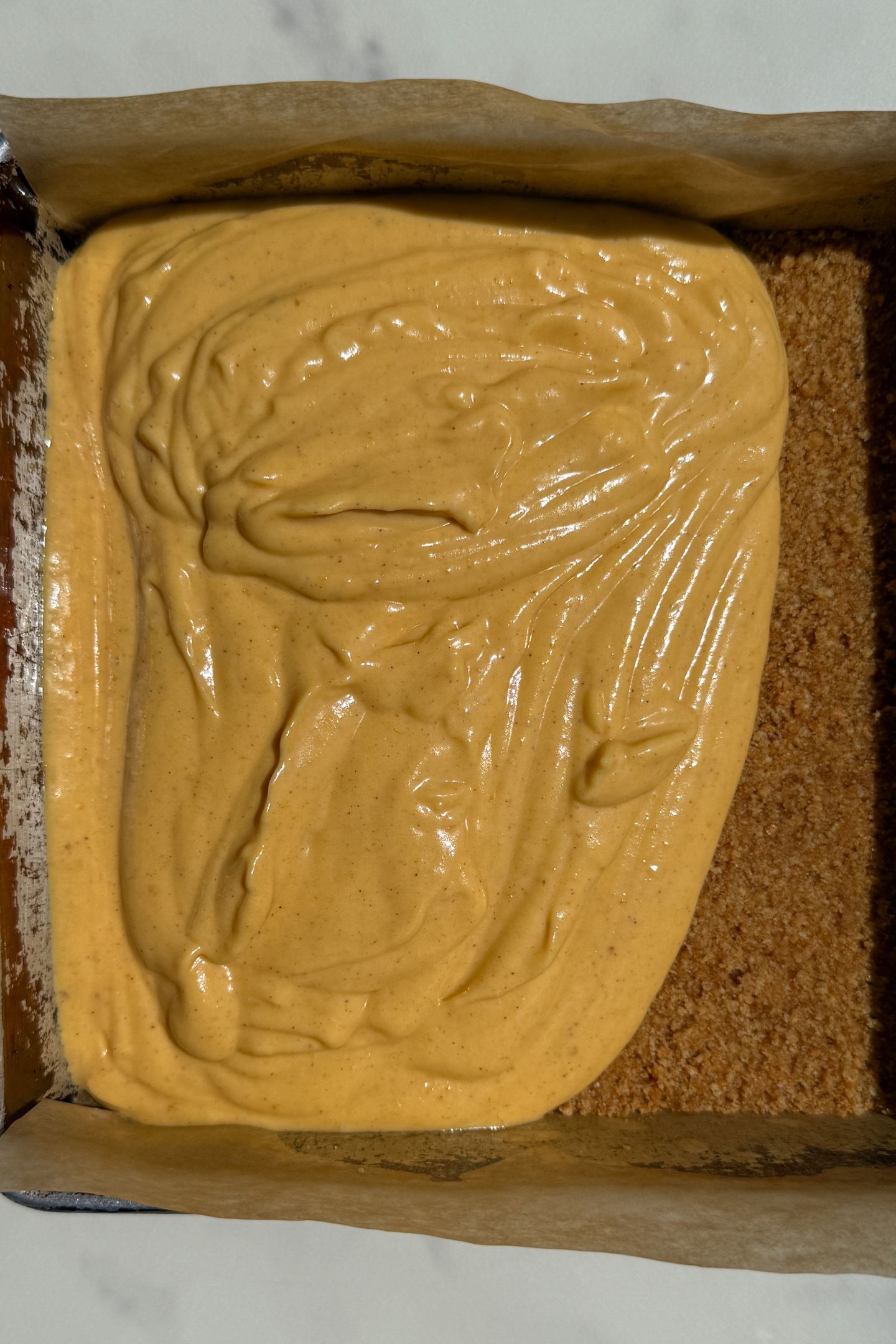 Cheesecake batter being added to the graham cracker crust.