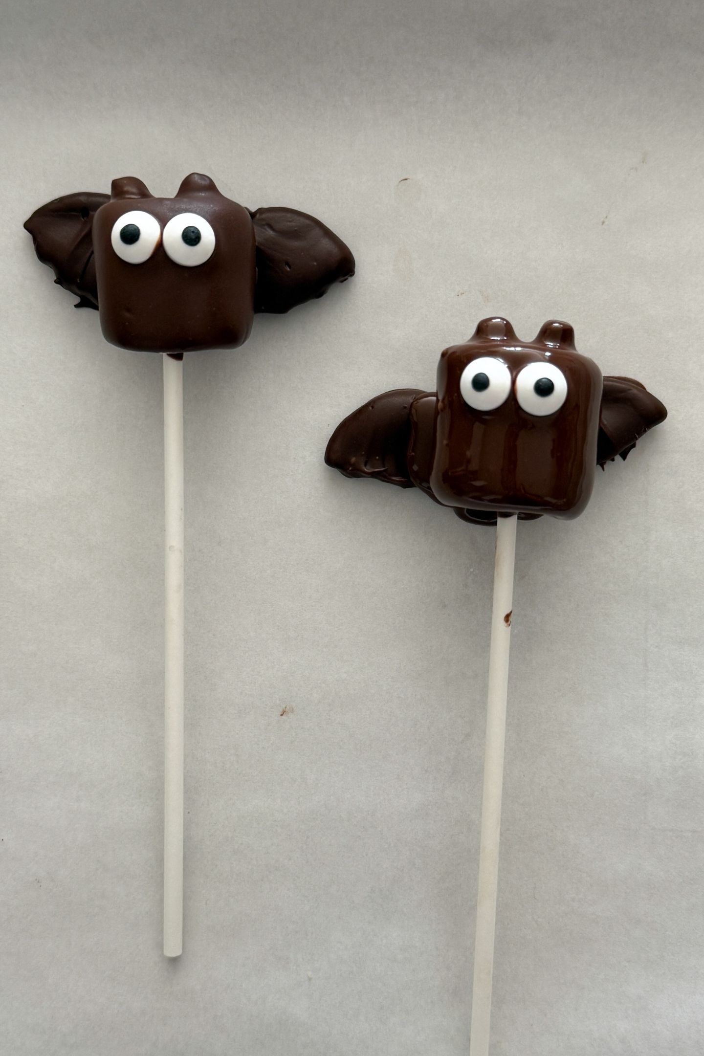 Assembling the bat marshmallow pops on a baking sheet lined with parchment paper.