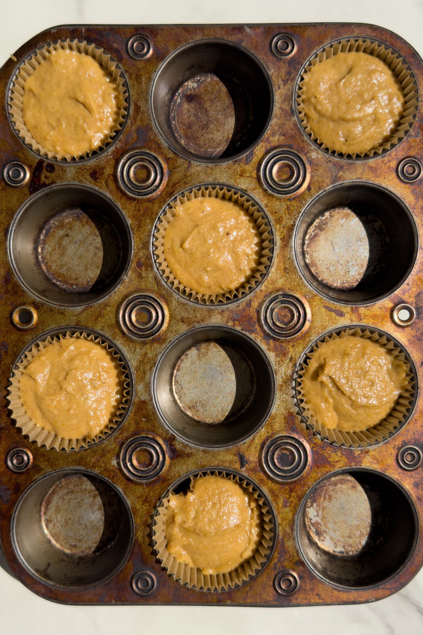 Scooping pumpkin banana bread muffin batter into the muffin liners.