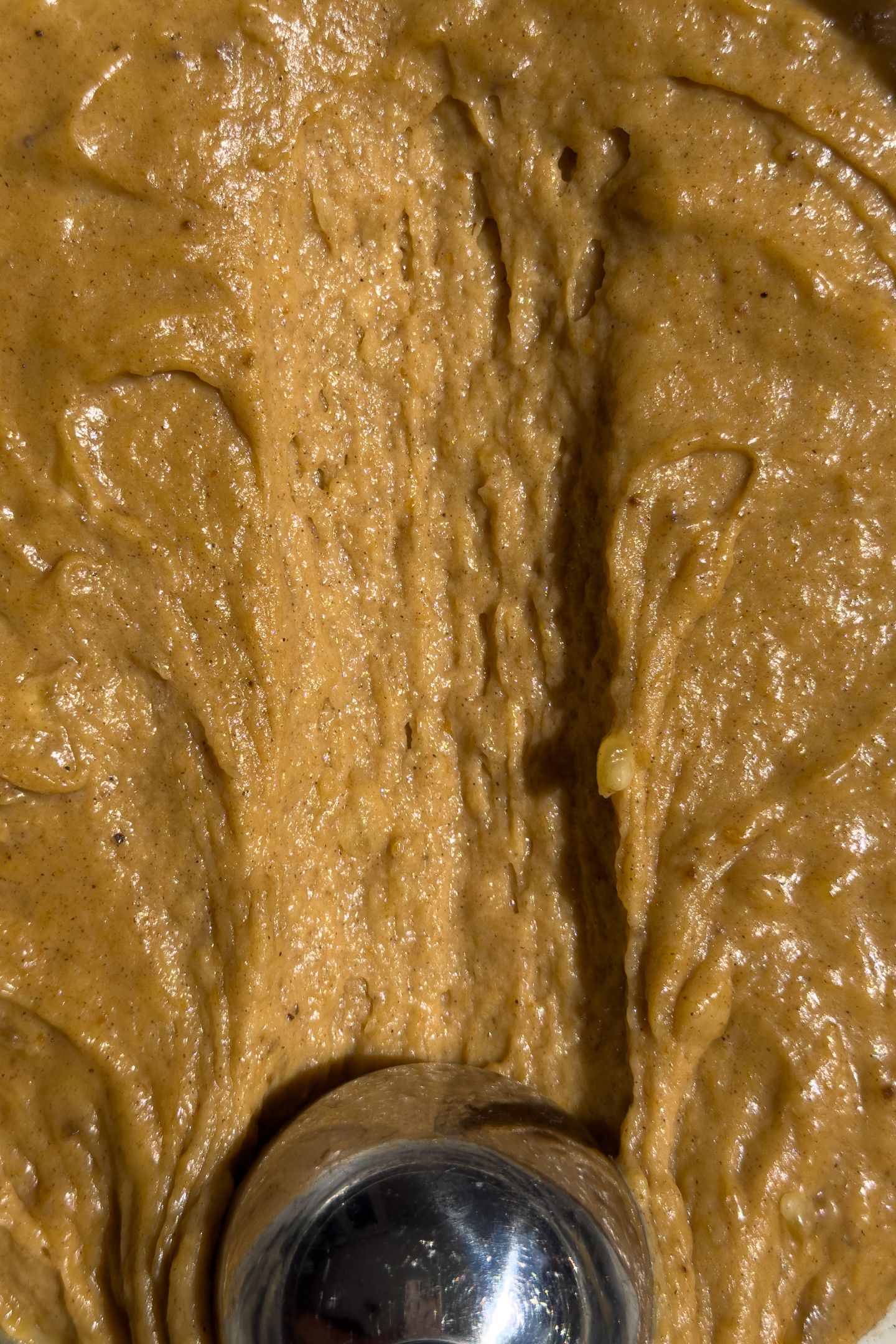 Scooping pumpkin banana bread muffin batter in a bowl.