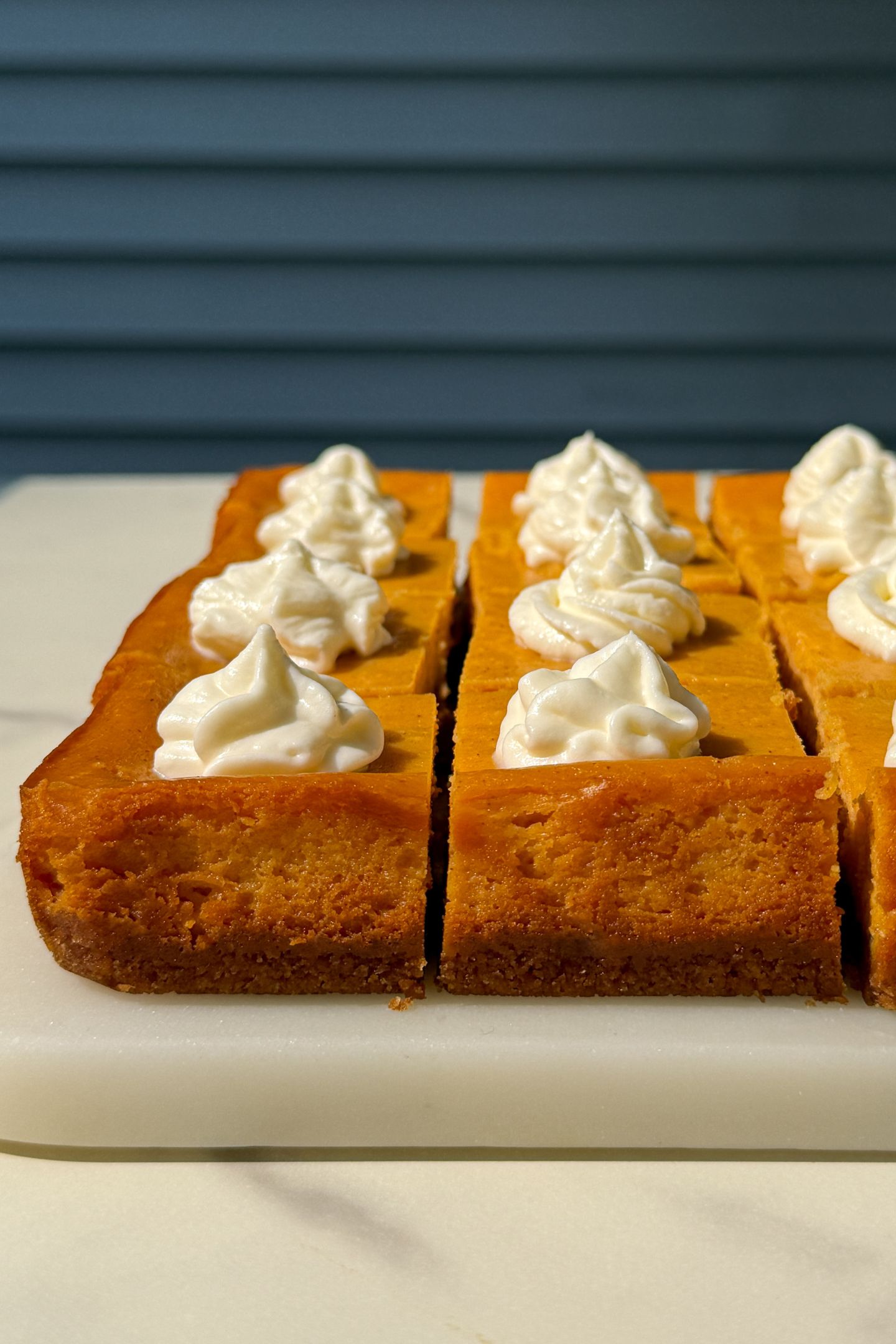 Pumpkin cheesecake bars on a platter and topped with whipped cream.