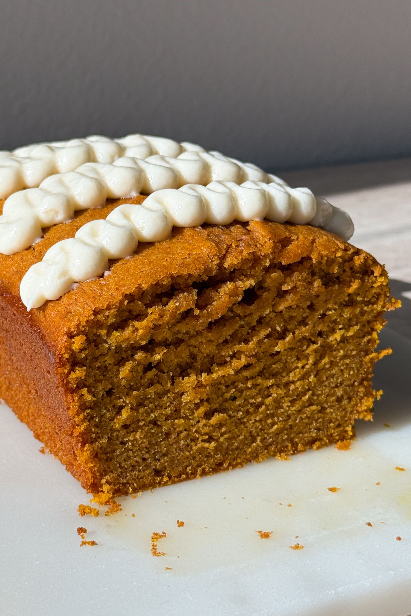Side view slicing the pumpkin bread with cream cheese frosting on top.
