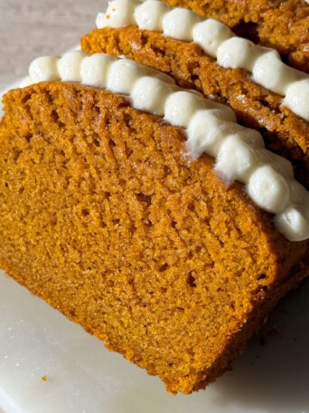 Slices of pumpkin bread topped with cream cheese frosting leaning on each other.