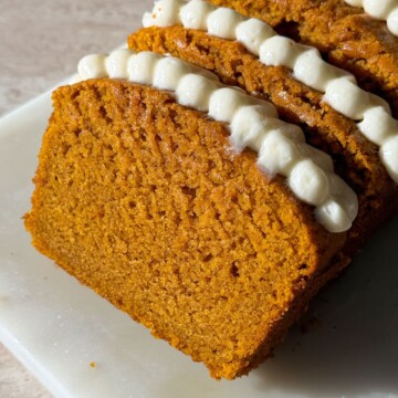 Slices of pumpkin bread topped with cream cheese frosting leaning on each other.