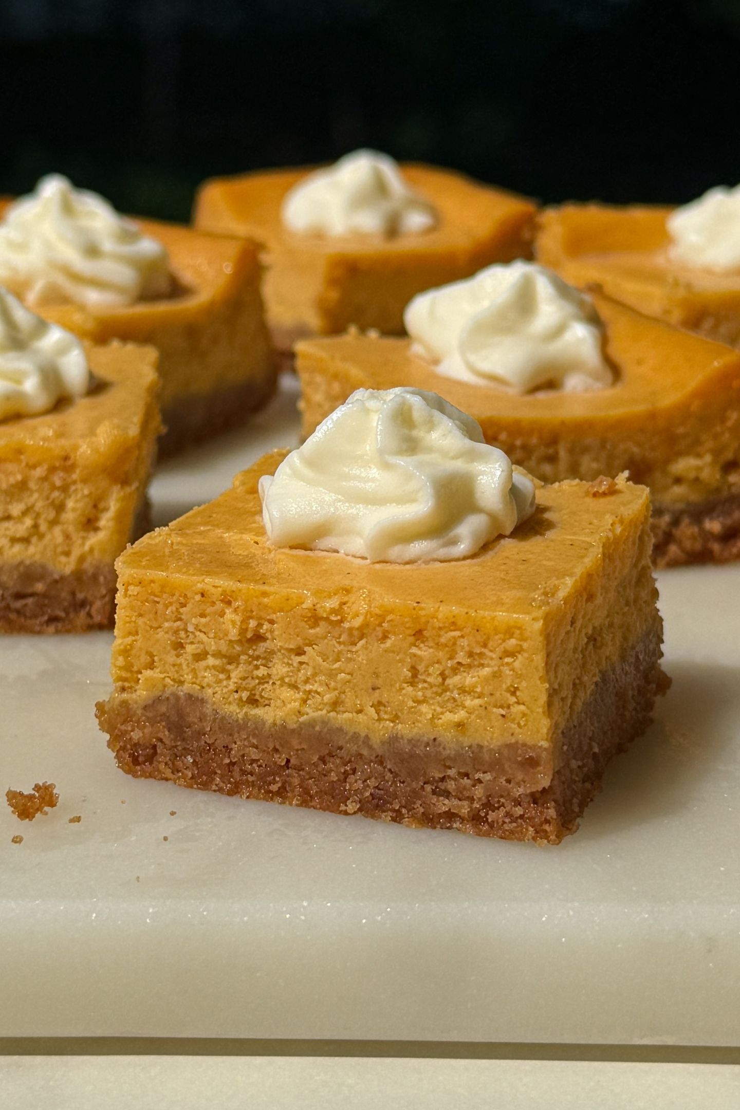 Pumpkin cheesecake bars on a platter topped with whipped cream.