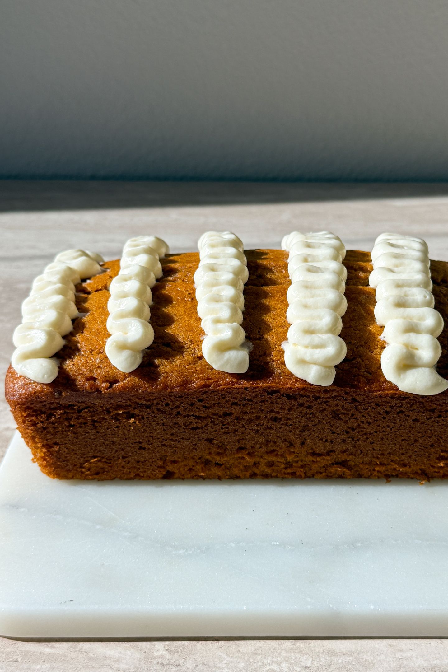 Adding cream cheese frosting to the top of the pumpkin bread.