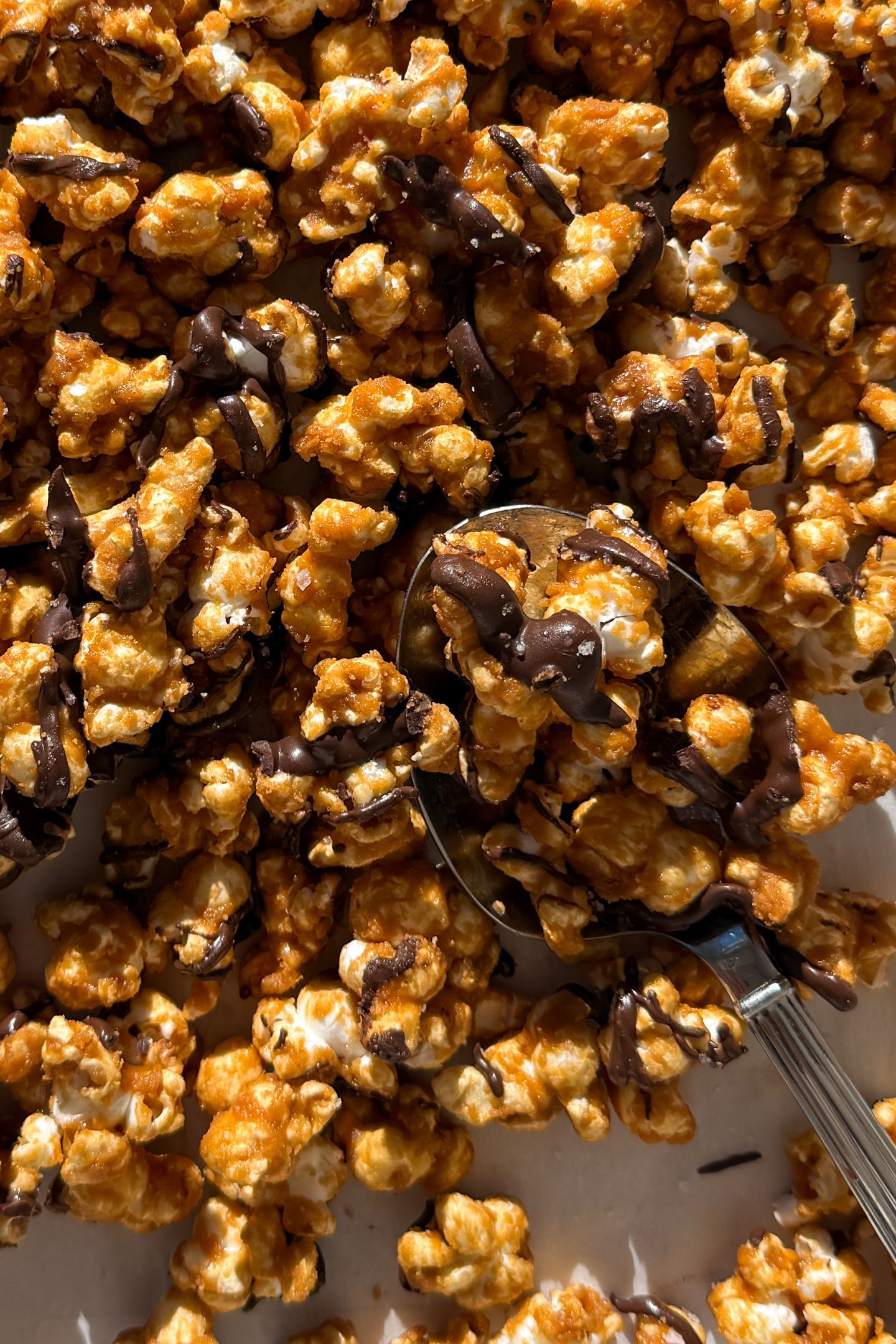 Homemade caramel popcorn drizzle with chocolate on a baking sheet that is lined with parchment paper.