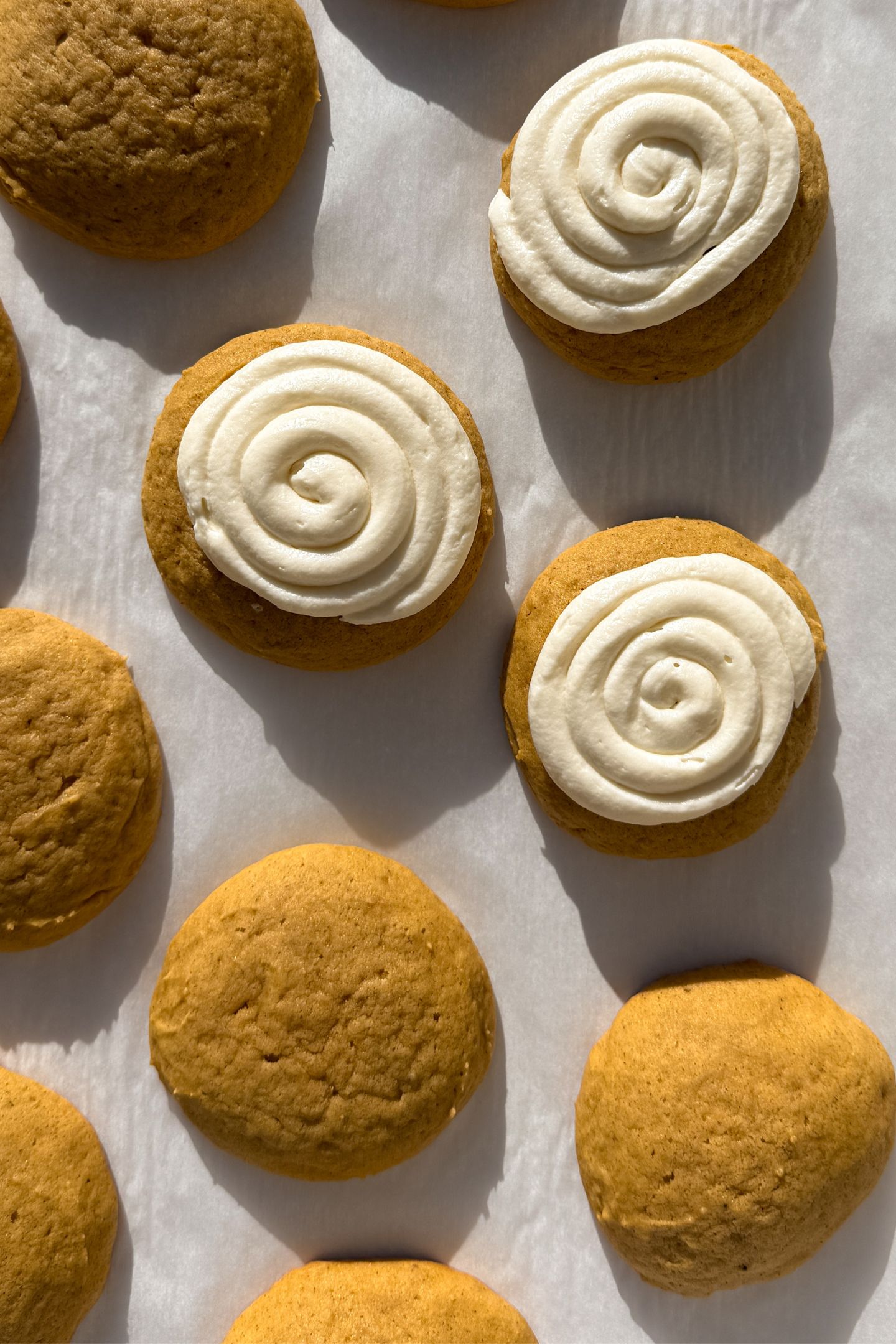 Frosting the pumpkin cookies on parchment paper.