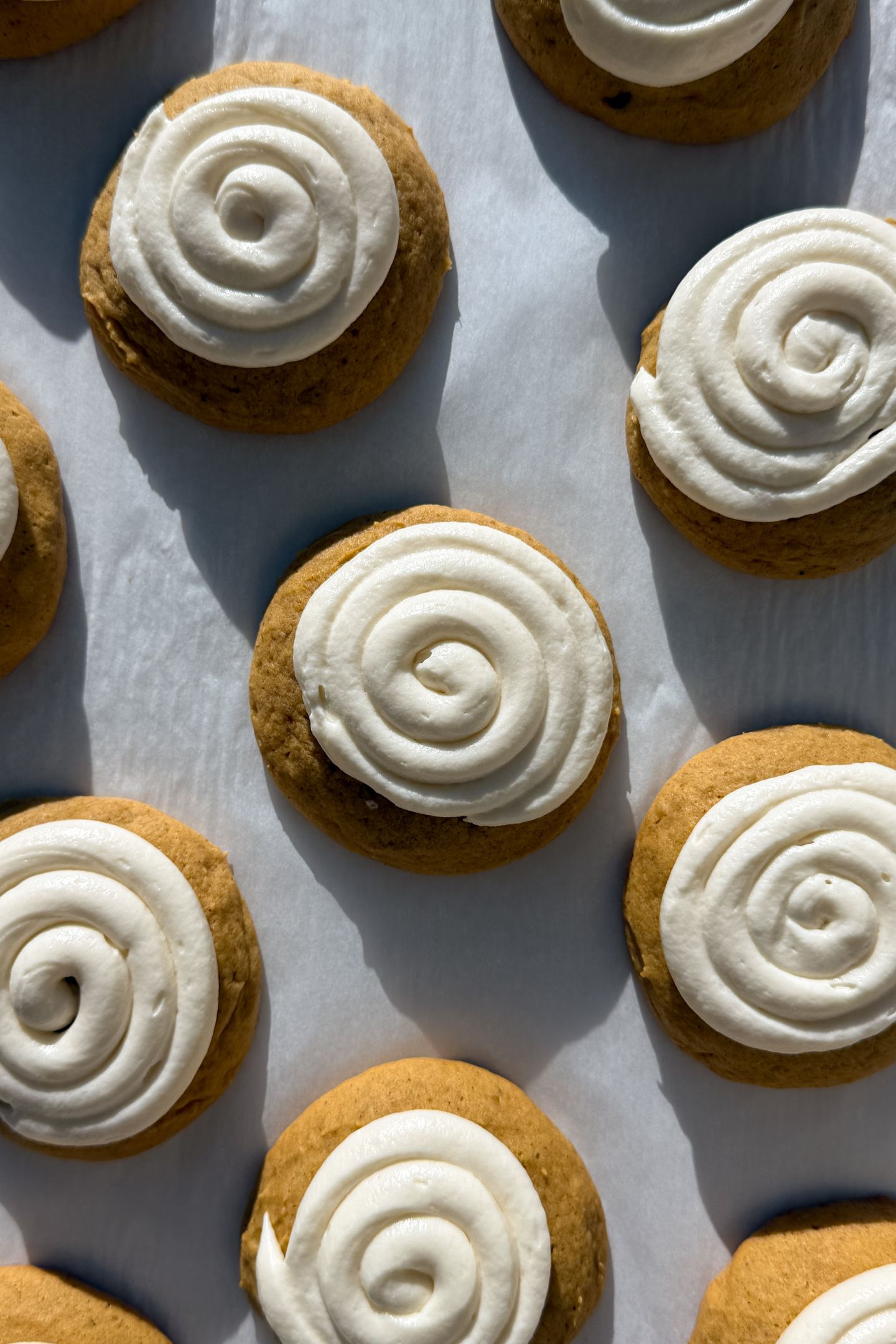 Frosted pumpkin cookies on a baking sheet lined with parchment paper.
