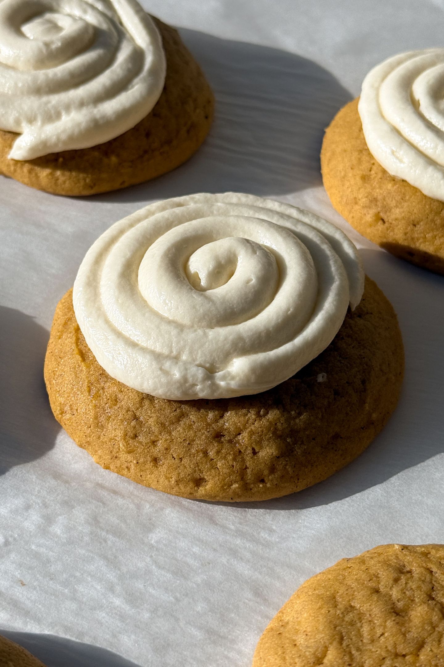Soft Pumpkin Cookie topped with Vanilla Cream Cheese Frosting on parchment paper.
