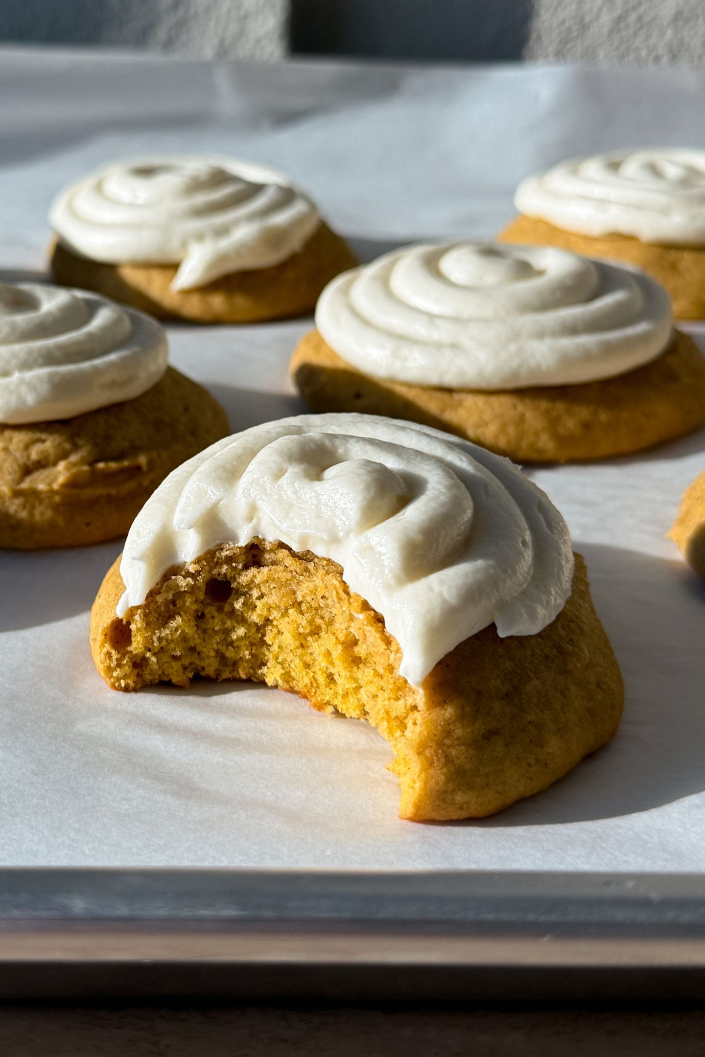 A frosted pumpkin cookie with a bite taken out of it.