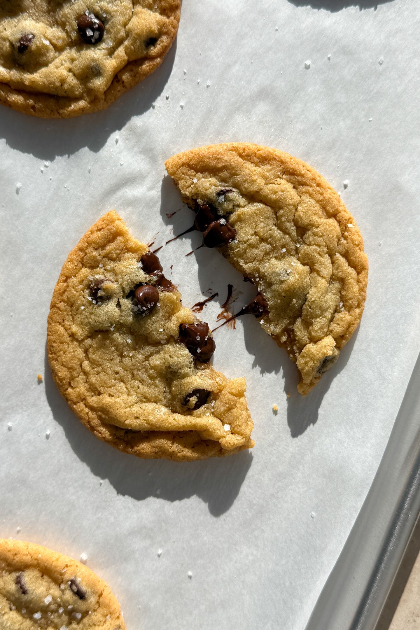A chocolate chip cookie broken in half on parchment paper.