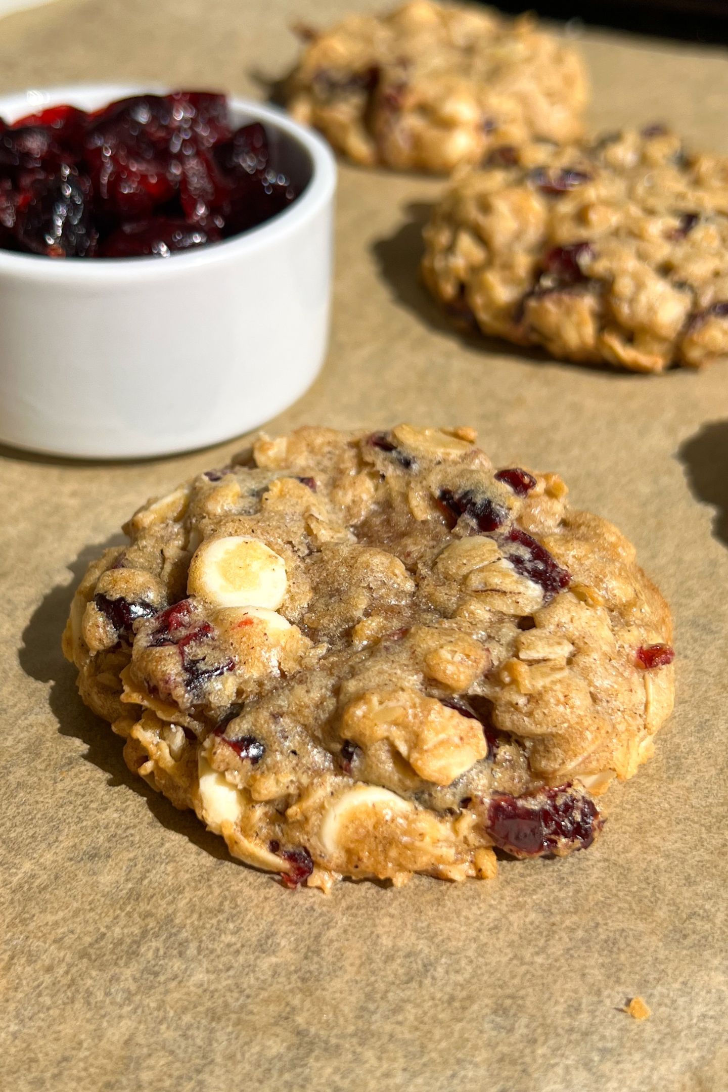 Side view of a White Chocolate Dried Cranberry Oatmeal Cookies on a baking sheet lined with parchment paper.