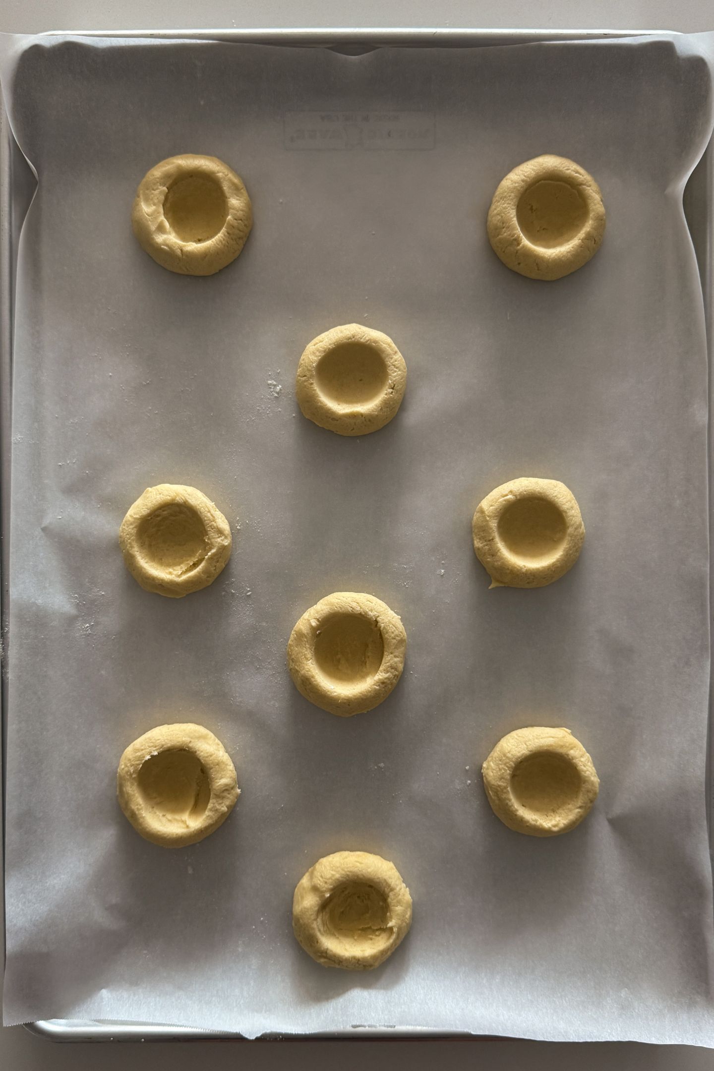 Cookie dough with divots in them on parchment paper ready to be baked.