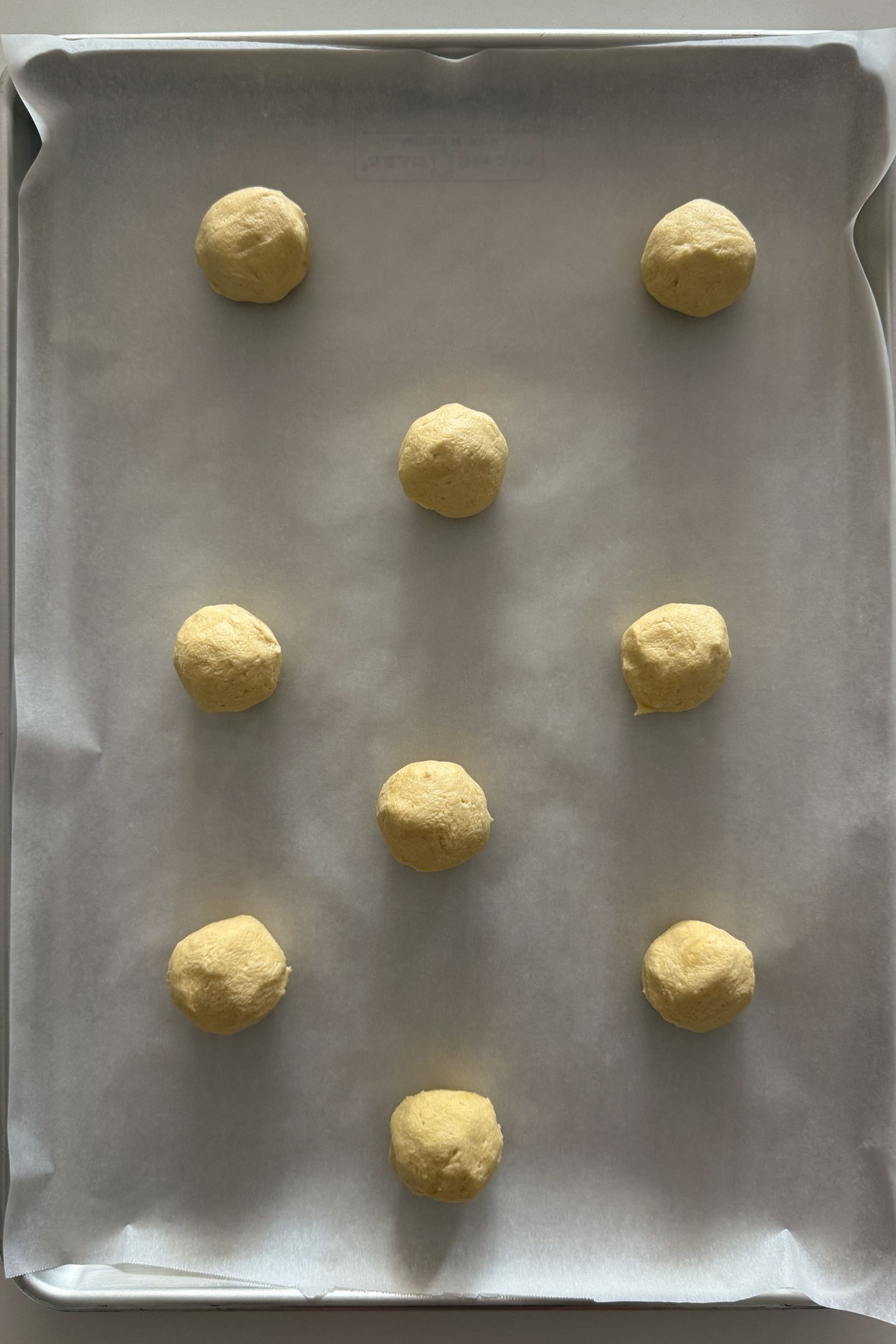 Cookie dough balls spread out on a baking sheet lined with parchment paper.