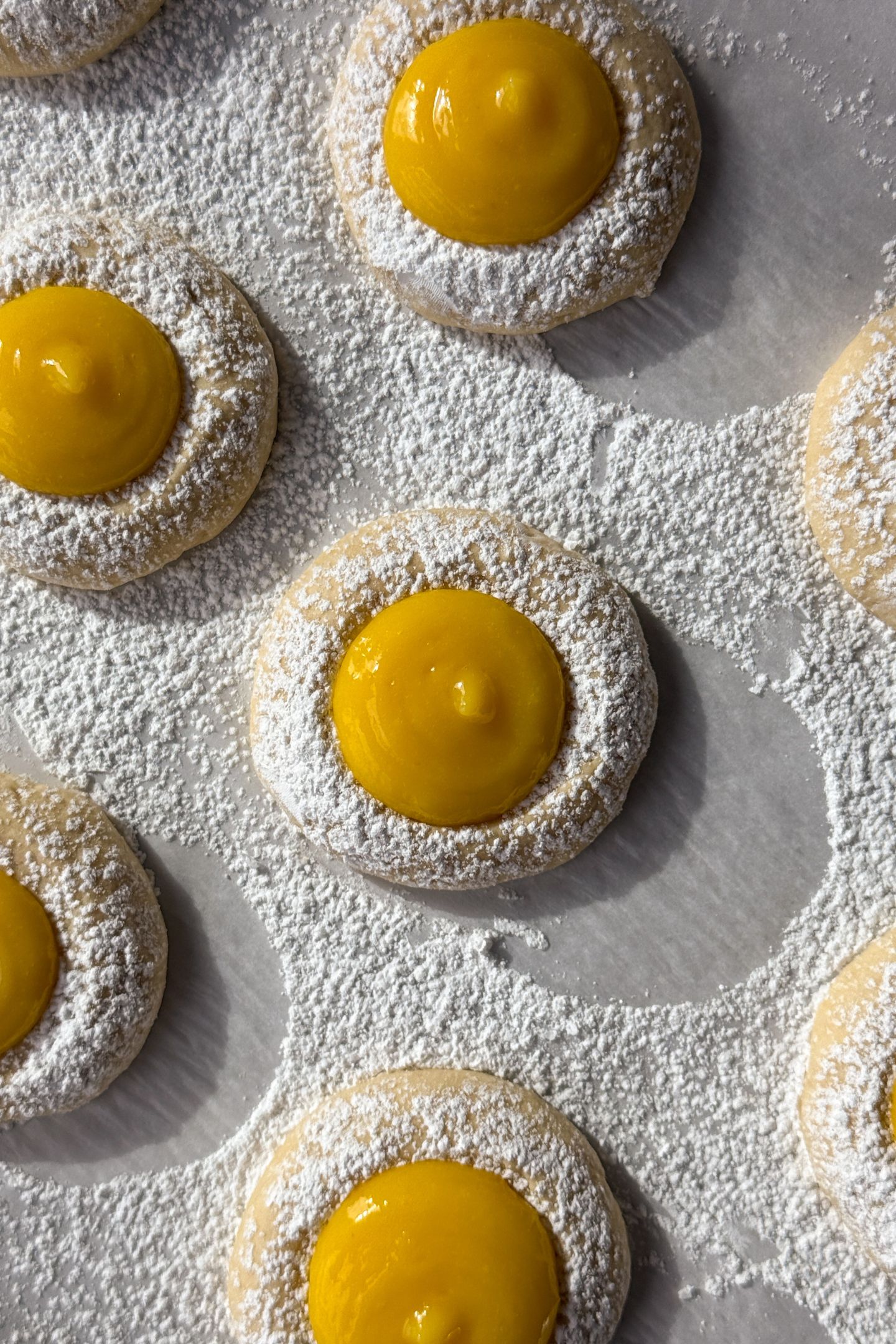 Lemon curd cookies on parchment paper dusted with powdered sugar.
