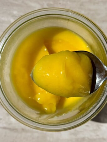 Lemon curd in a spoon over a mason jar.