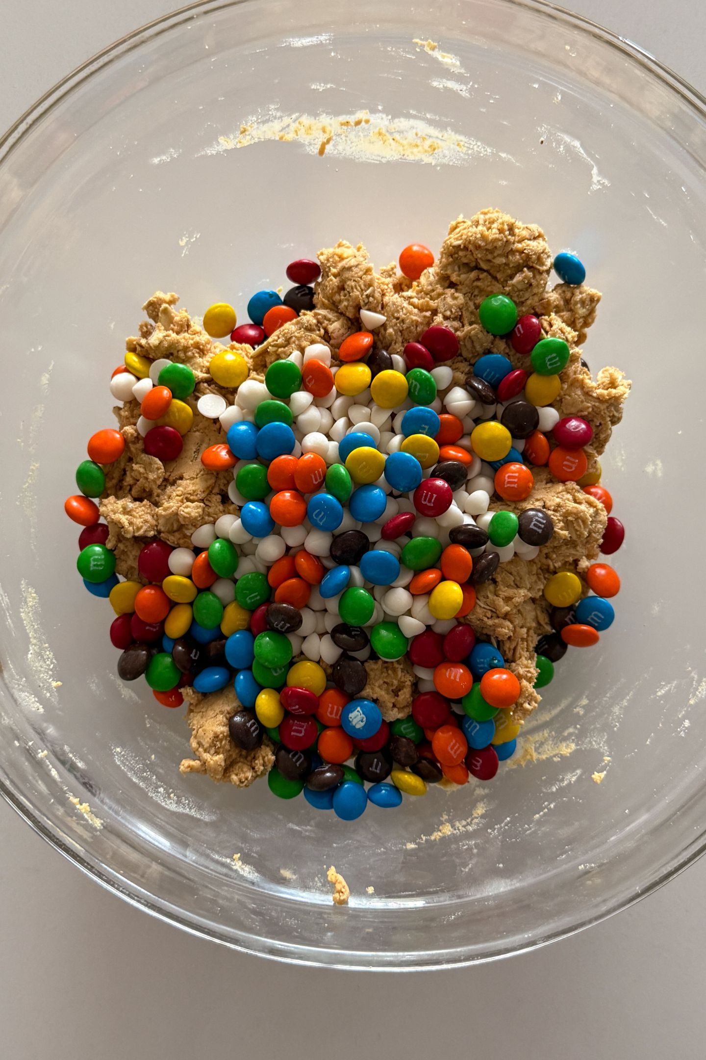 Adding mini m and m candies to the peanut butter oat dough in a bowl.