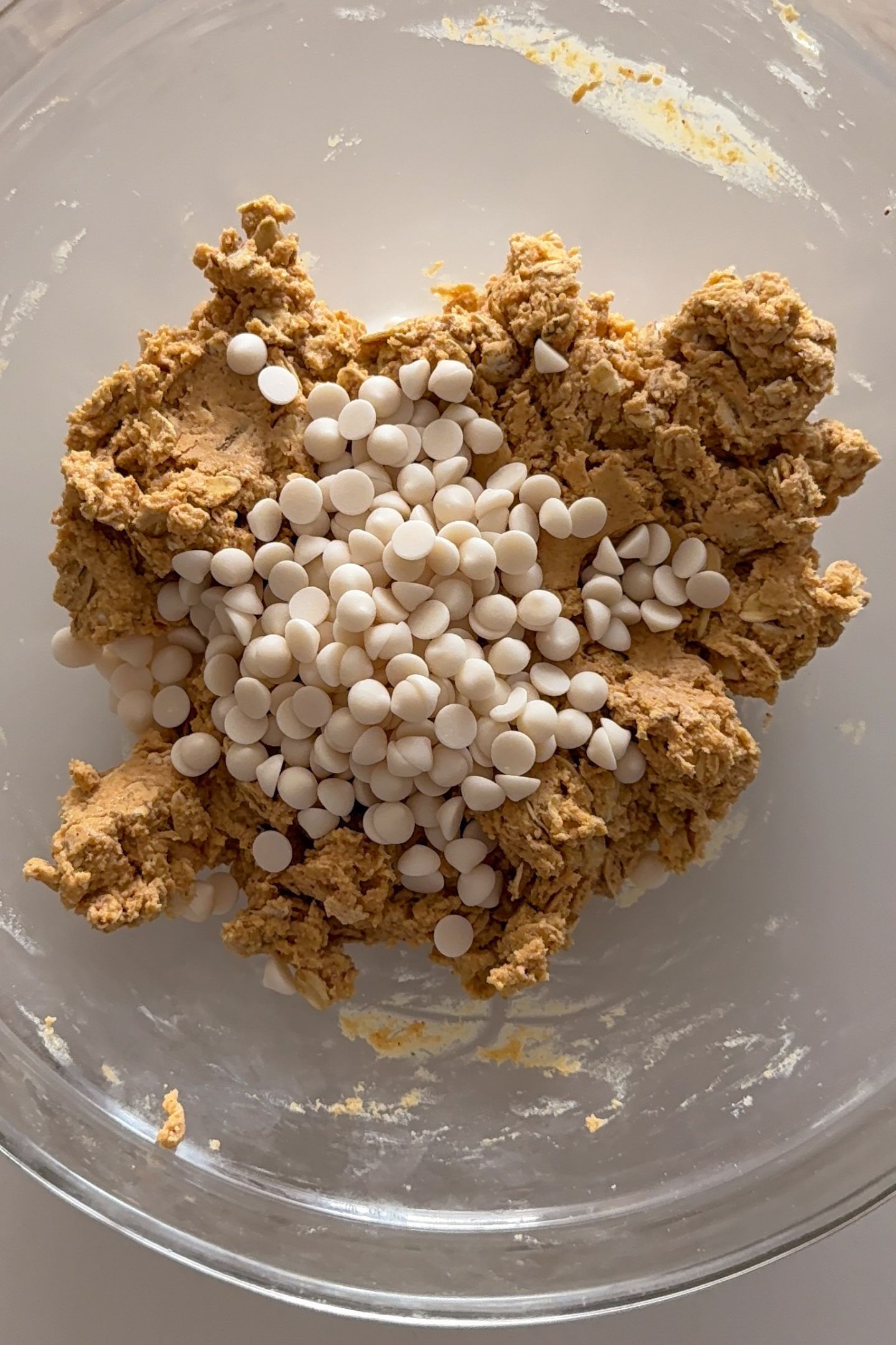 Adding mini white chocolate chips to the peanut butter oat dough in a bowl.