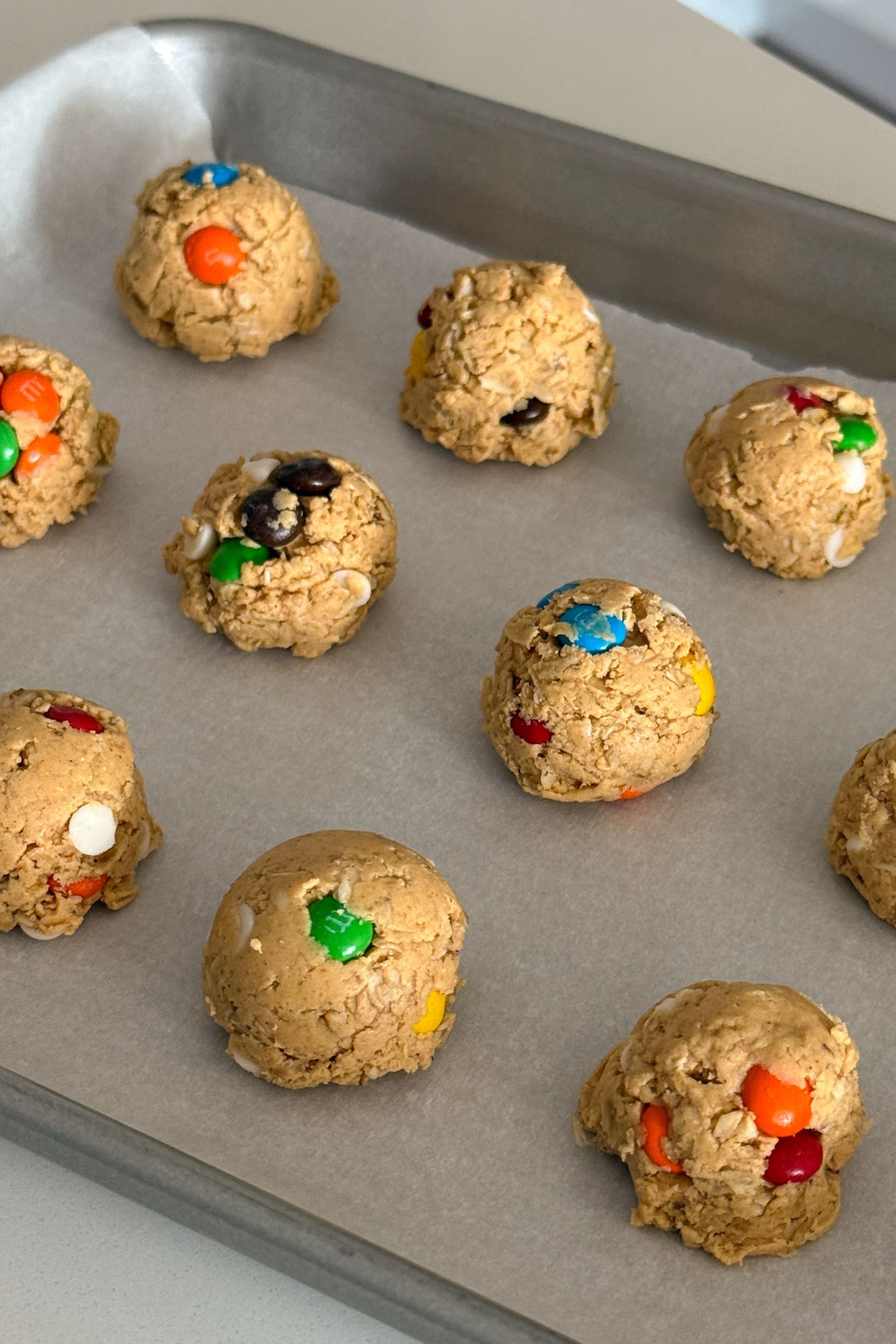 Monster cookie balls on a baking sheet lined with parchment paper.