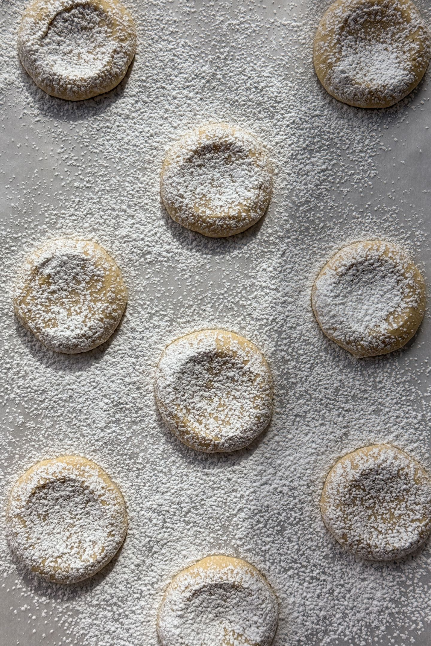 Cookies dusted in powdered sugar on parchment paper.