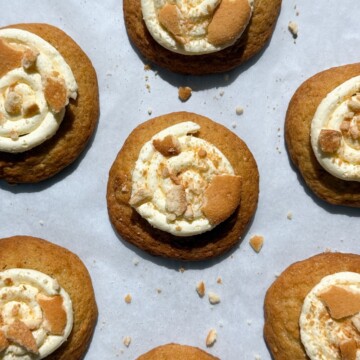 Banana Pudding Cookies topped with frosting and crushed wafer cookies on parchment paper.