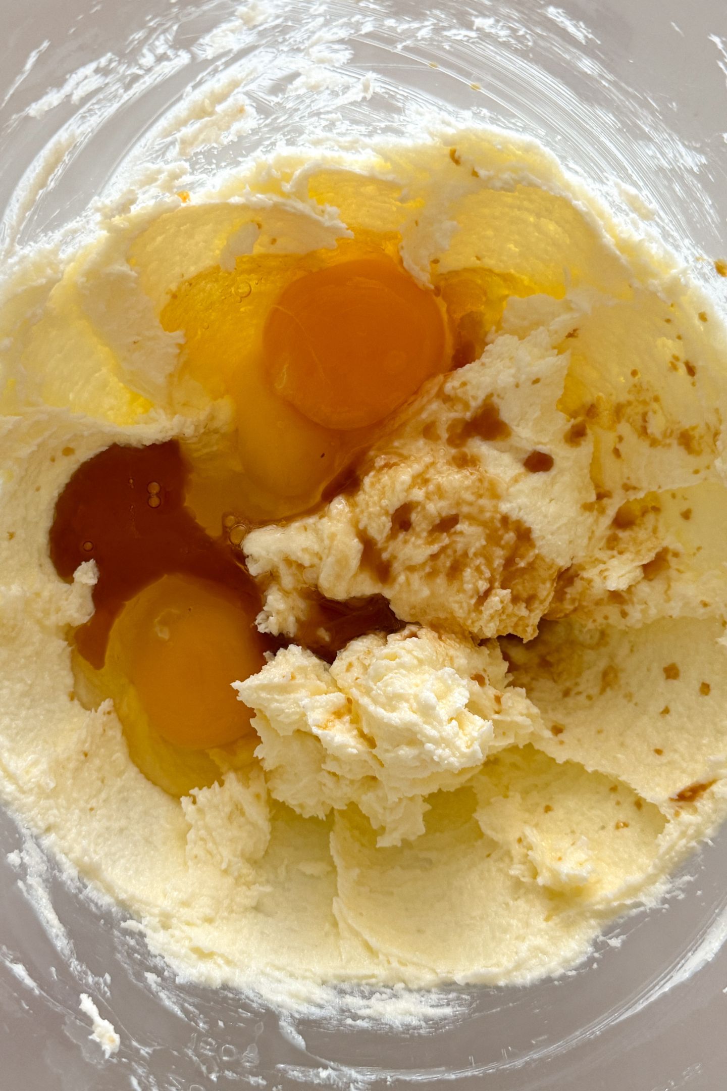 Adding eggs and vanilla extract to softened butter and granulated sugar that has been combined together in a bowl.