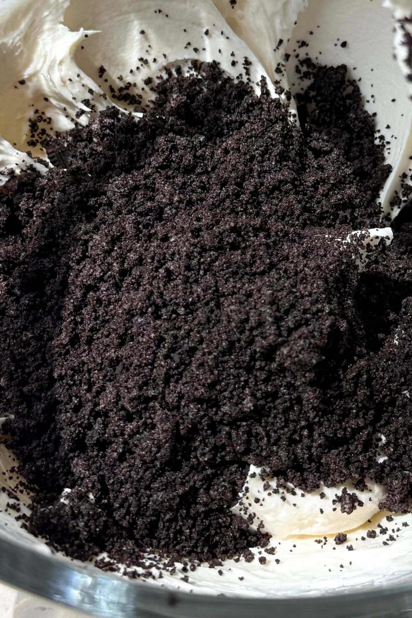 Adding the crushed oreo cookies to the base of the oreo buttercream frosting in a stand mixer.