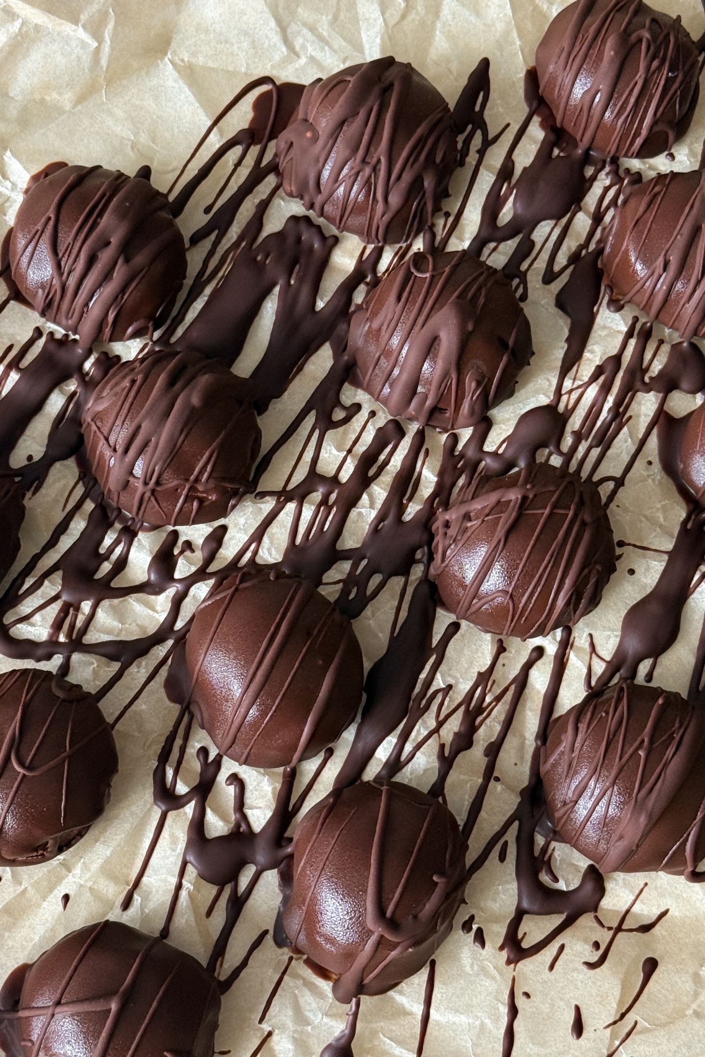 Frozen Cheesecake Bites Coated and Drizzled with Chocolate on a baking sheet that is lined with parchment.
