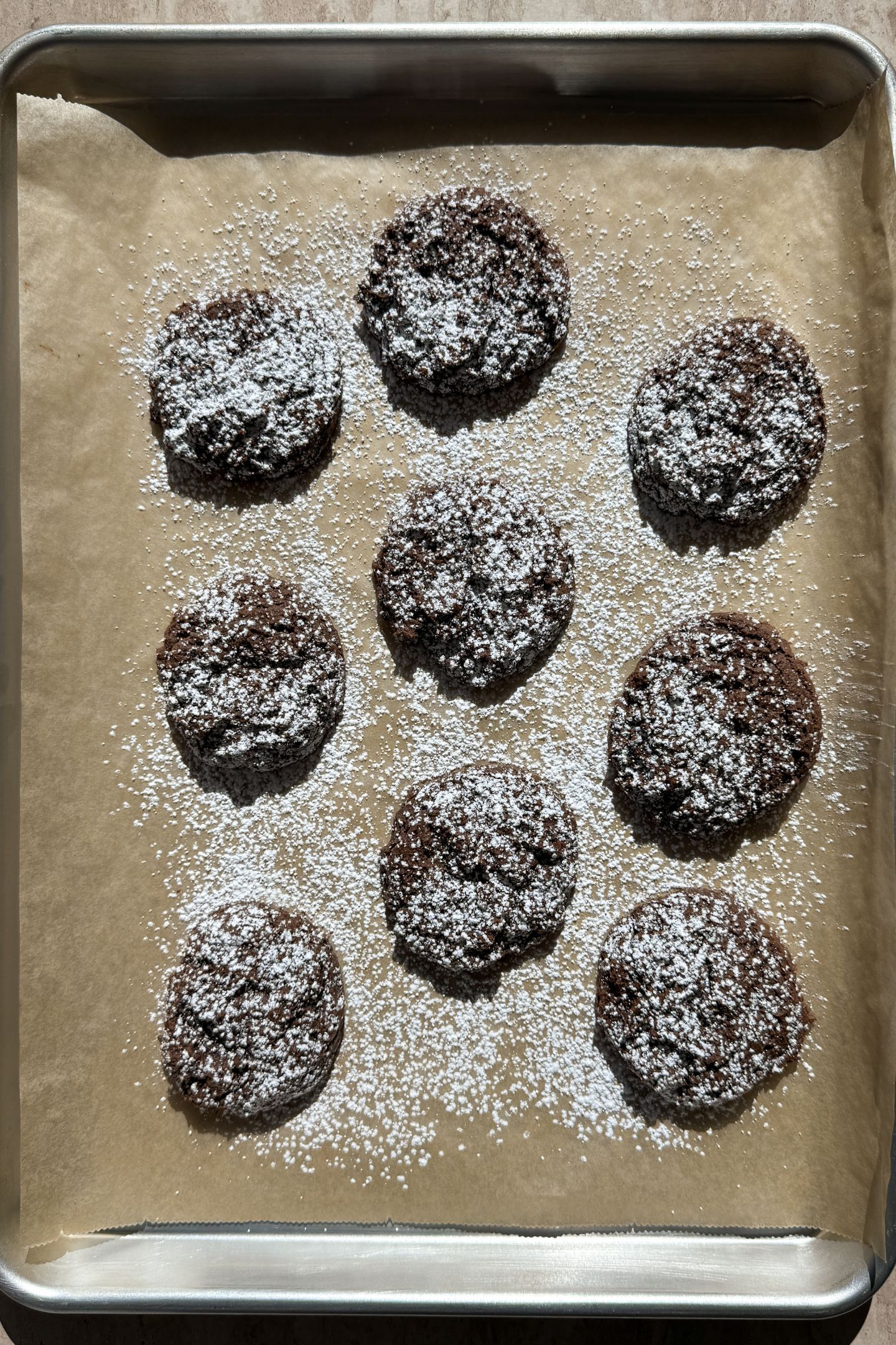 Baked cookies on a baking sheet lined with parchment paper that have been topped with powdered sugar.