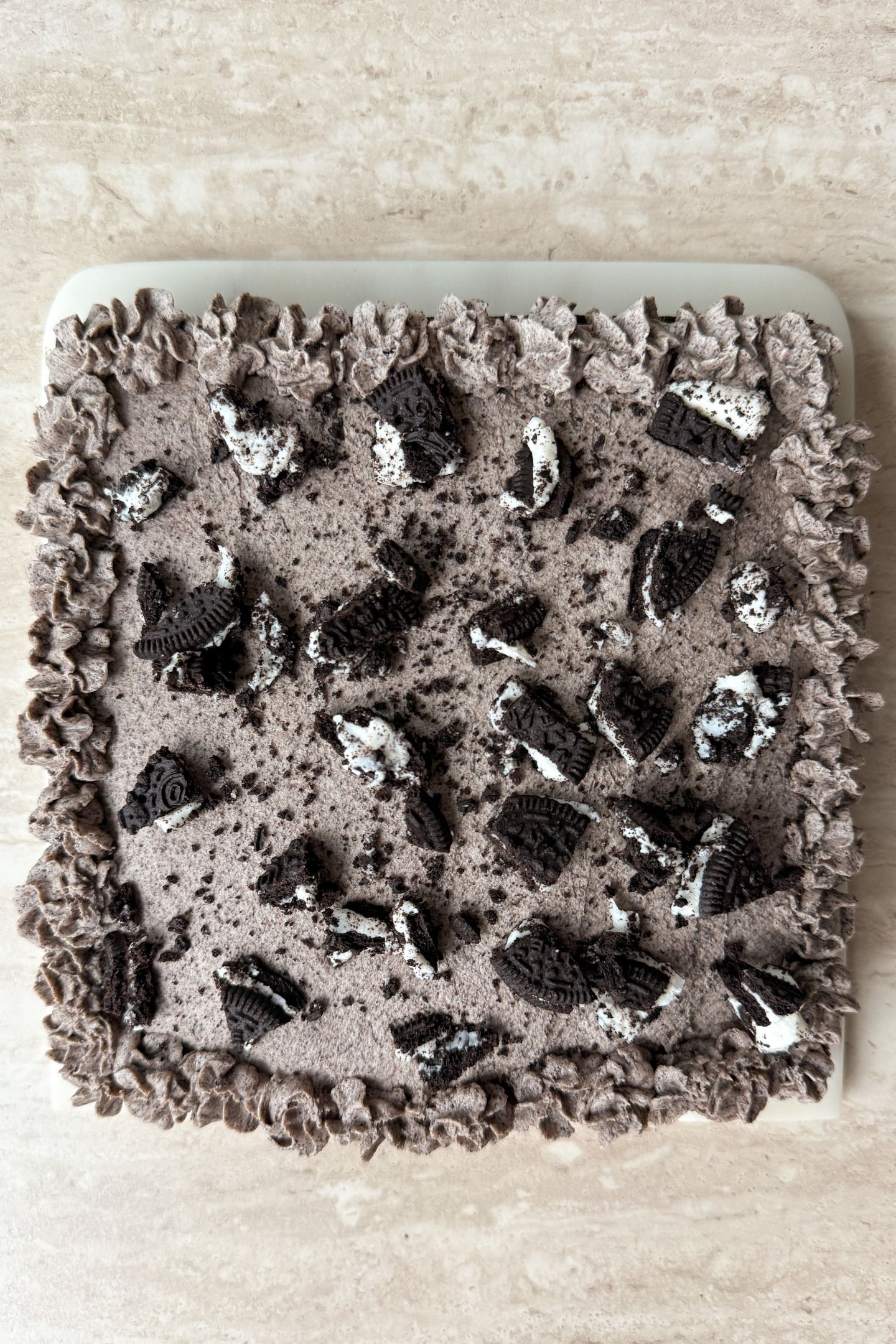 Adding the cookies and cream frosting on top of the chocolate cake along with crushed cookies.
