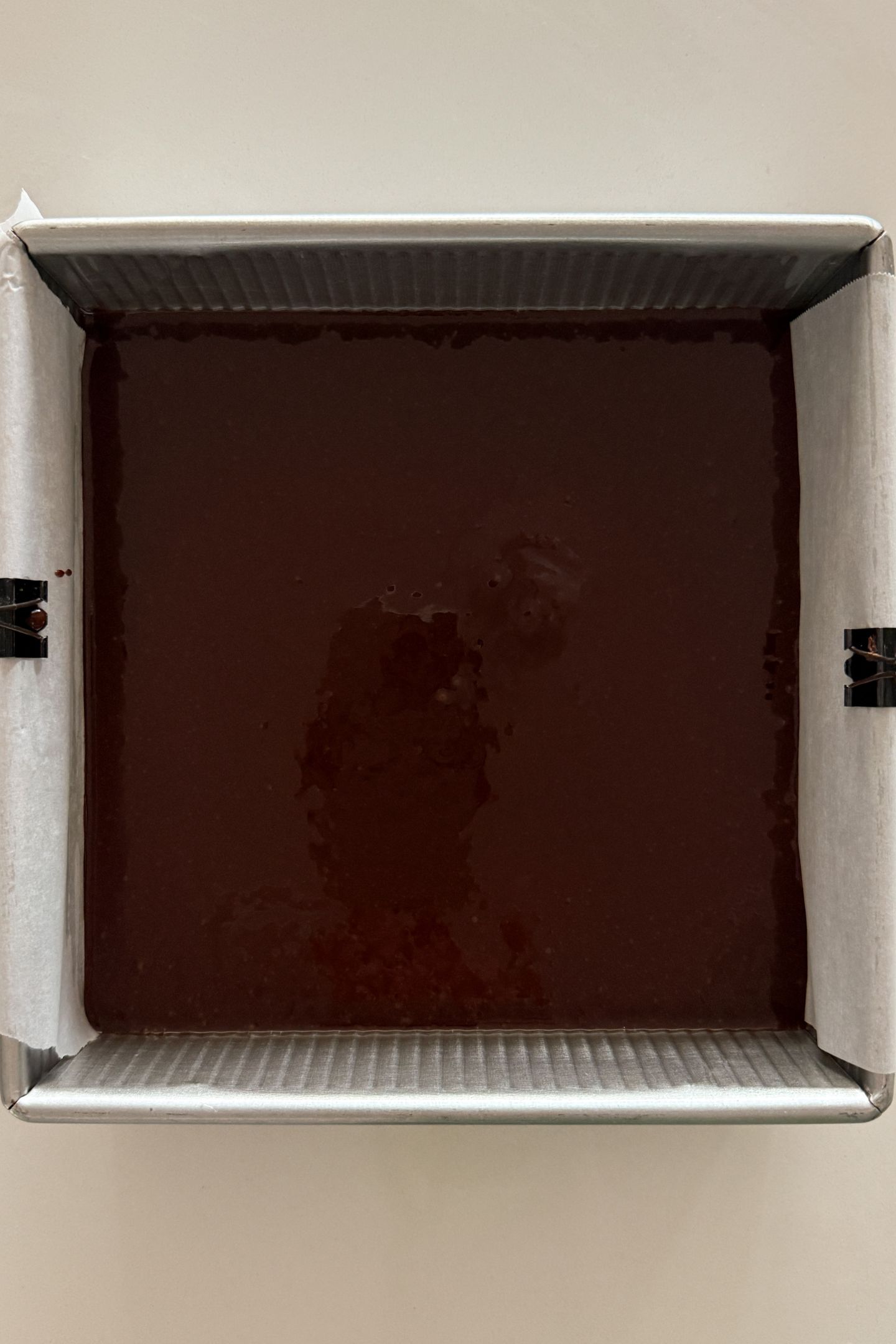 Chocolate cake batter in a prepared square baking pan.