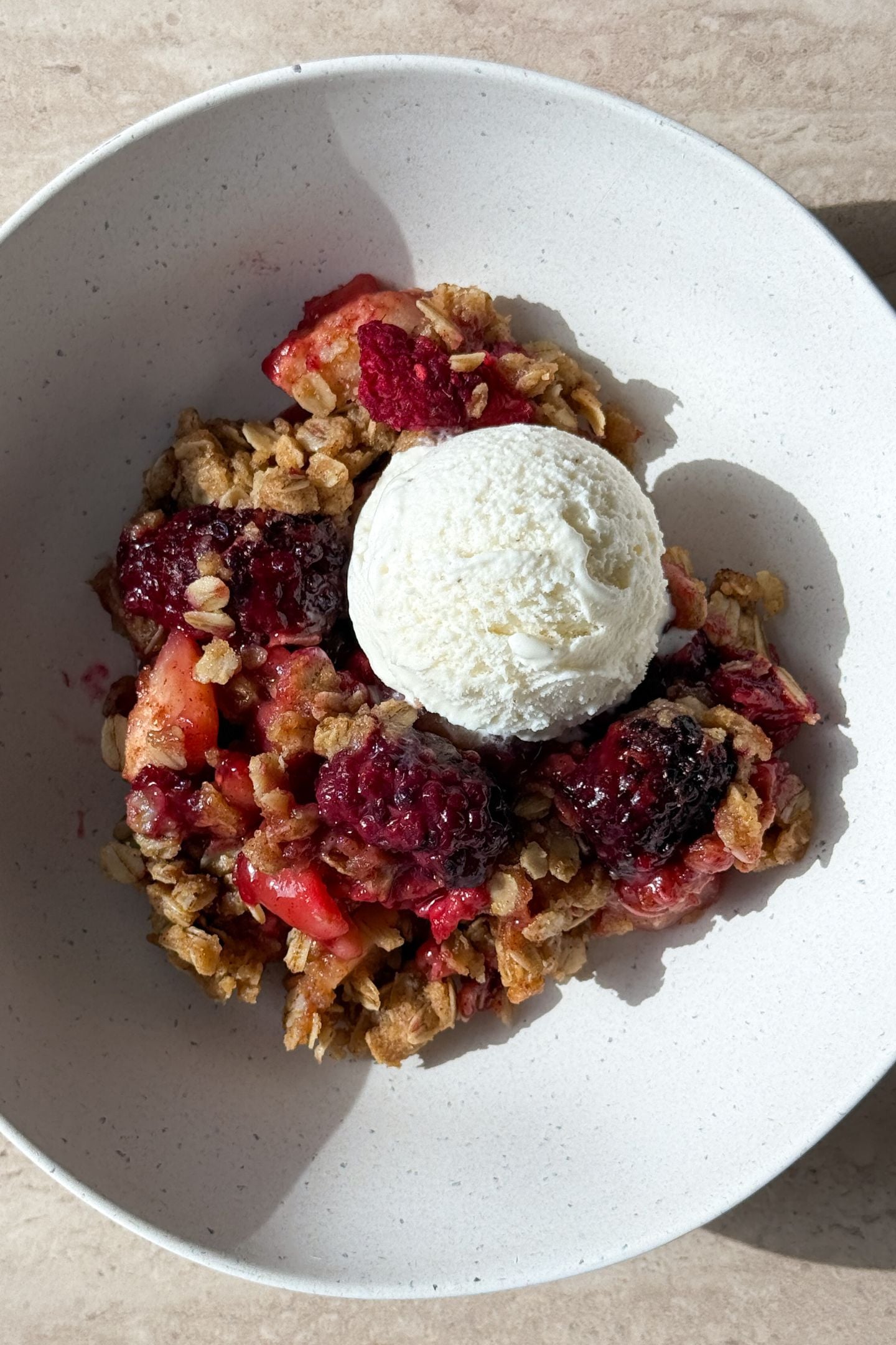 A serving of apple berry crisp in a bowl with vanilla ice cream.