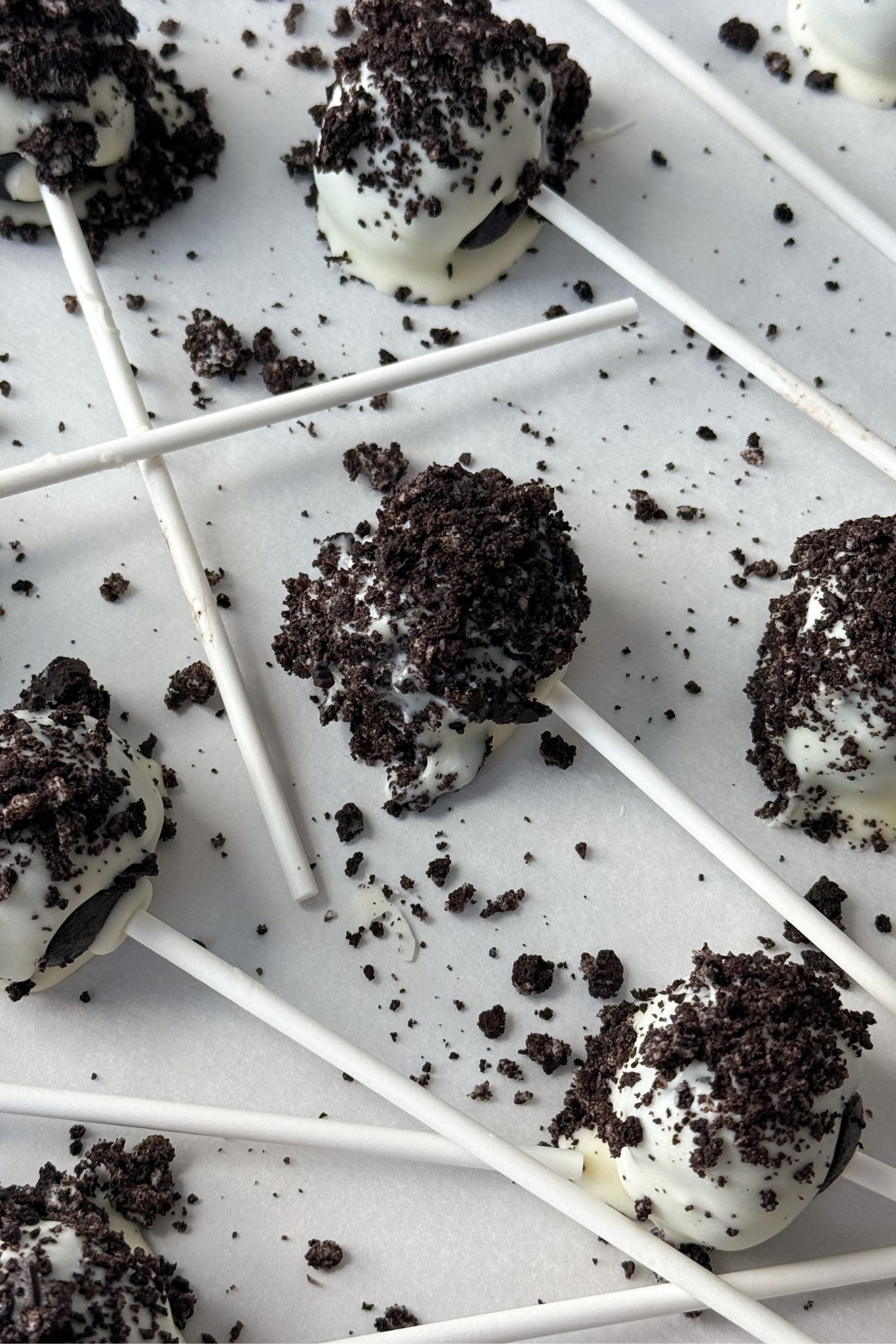 Cake pops coated in white chocolate and oreo chocolate sandwich crumbs on a baking sheet lined with parchment paper.