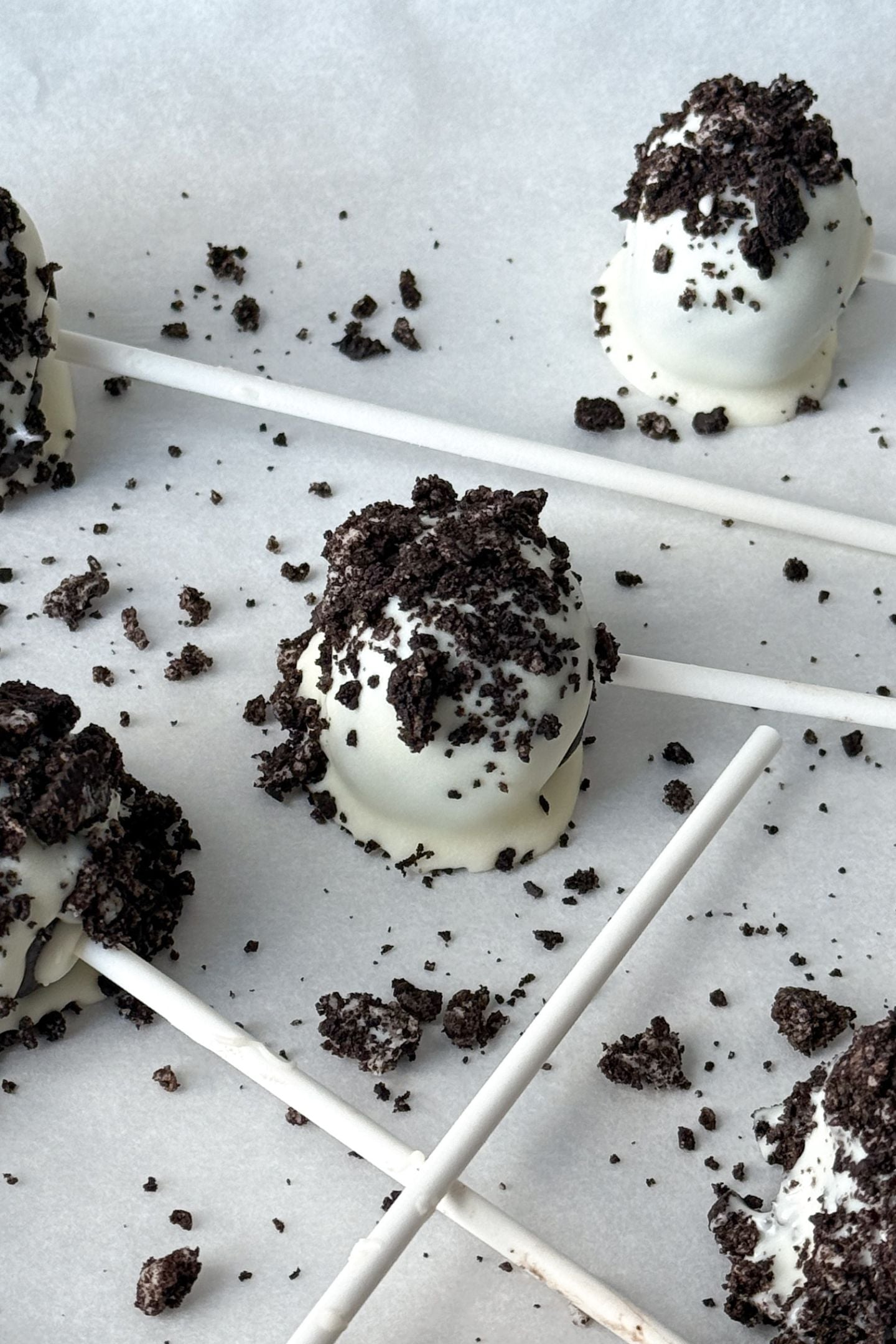 Cake pops coated in white chocolate and oreo chocolate sandwich crumbs on a baking sheet lined with parchment paper.